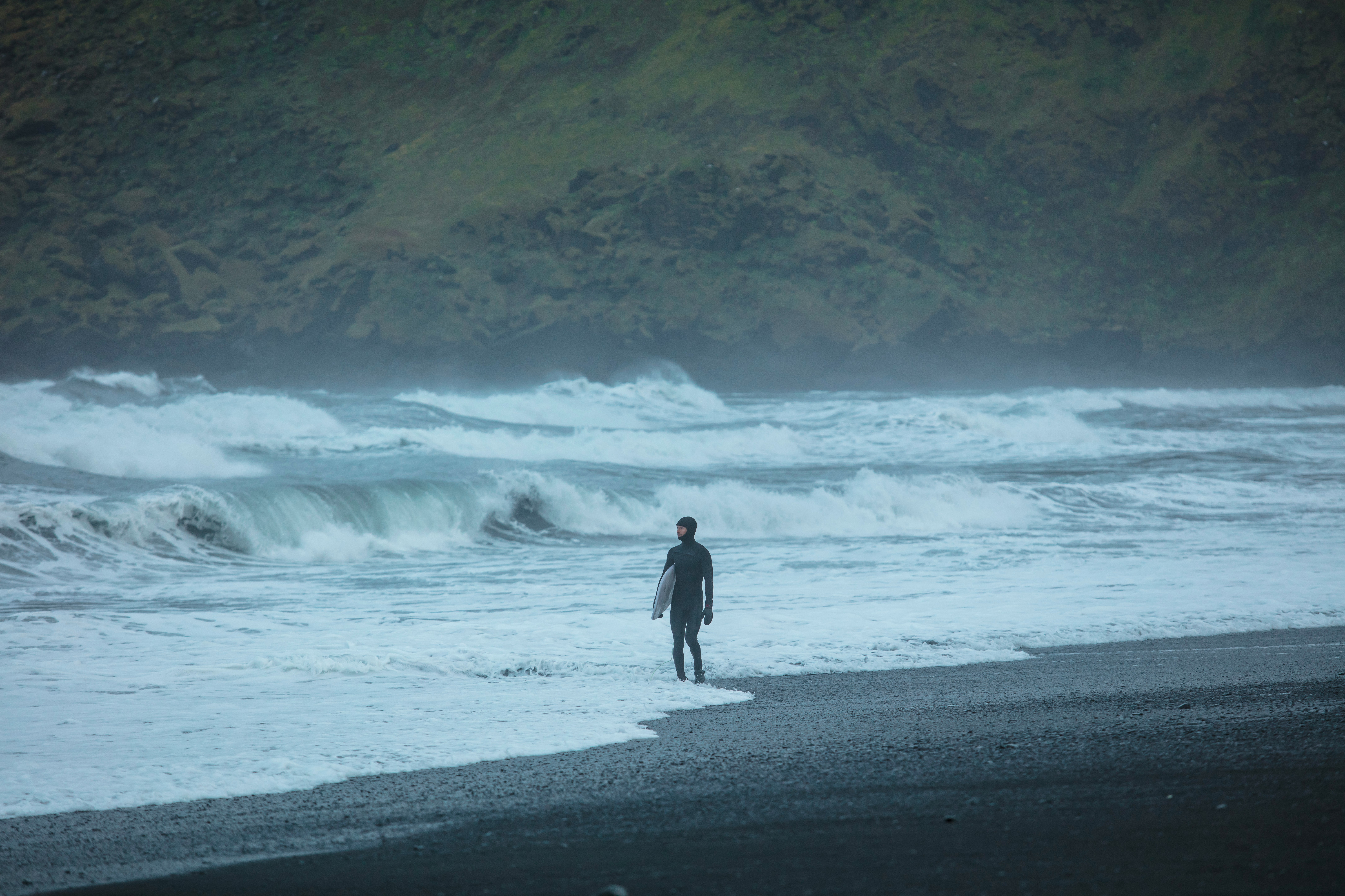Surfer standing on a black sand beach holding a surfboard.