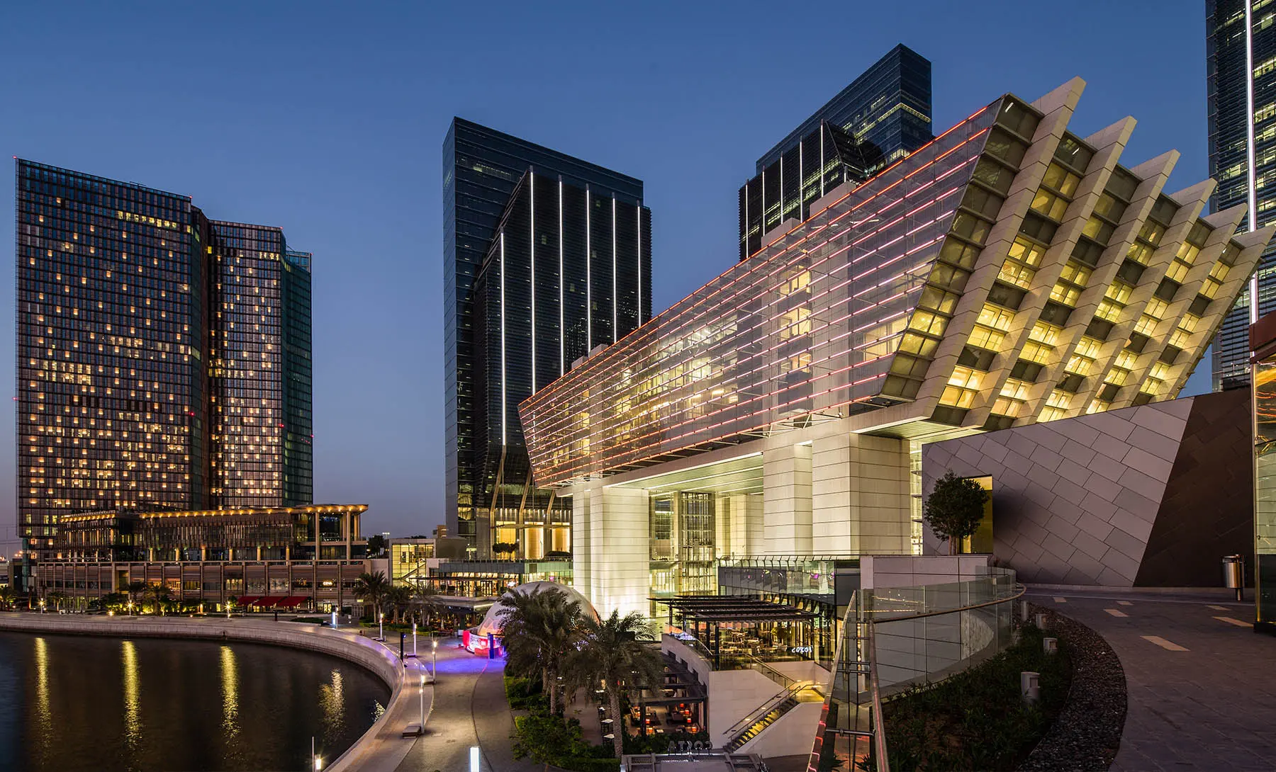 Modern office building with large windows reflecting a vivid orange sunset sky, silhouetted figure visible through the glass.