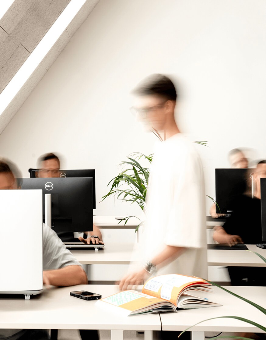 Motion blurred shot of a modern startup team working at desks in a bright, white office environment.