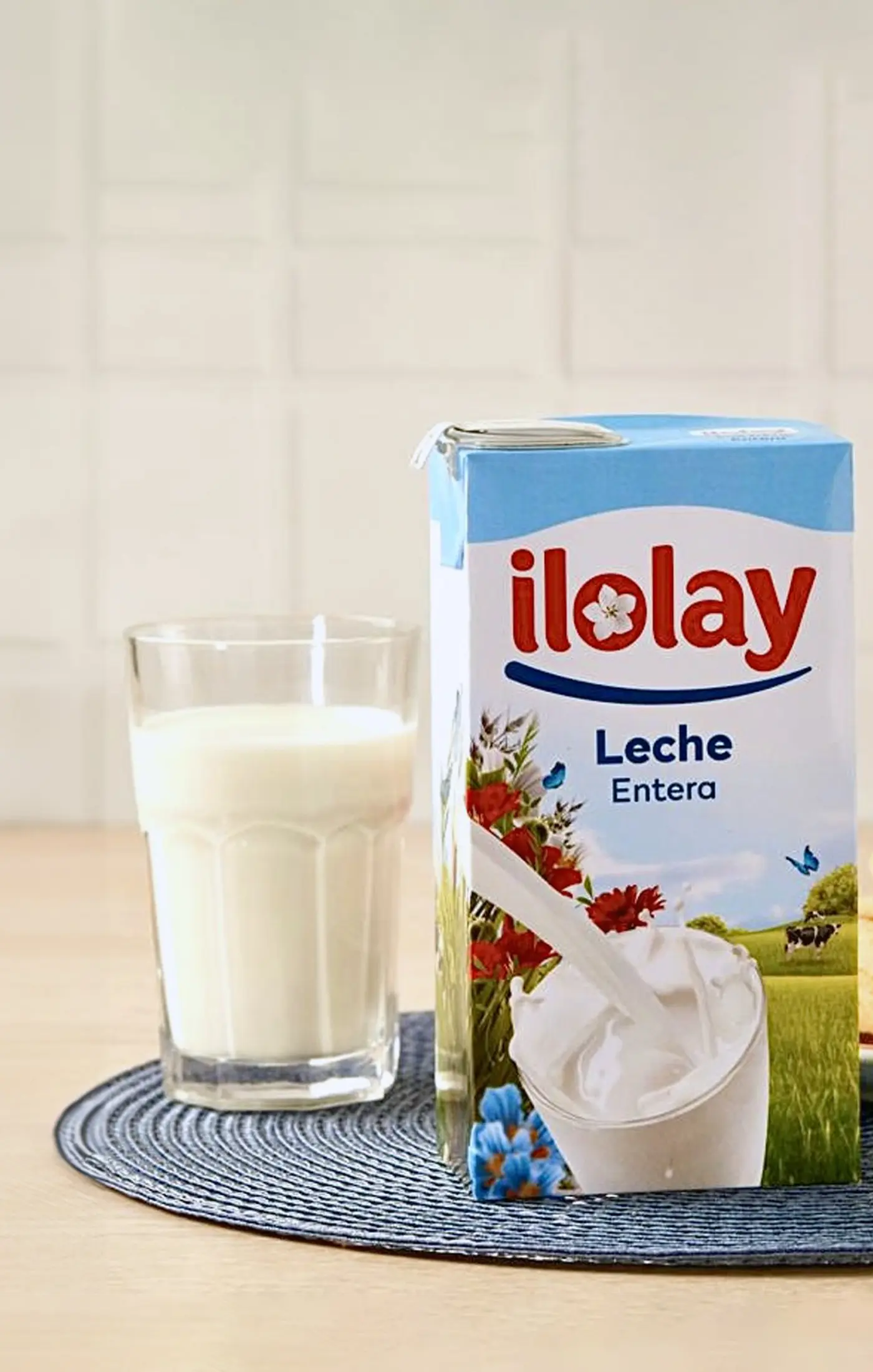 A carton of milk, a glass of milk, and a biscuit on a plate against a light background.