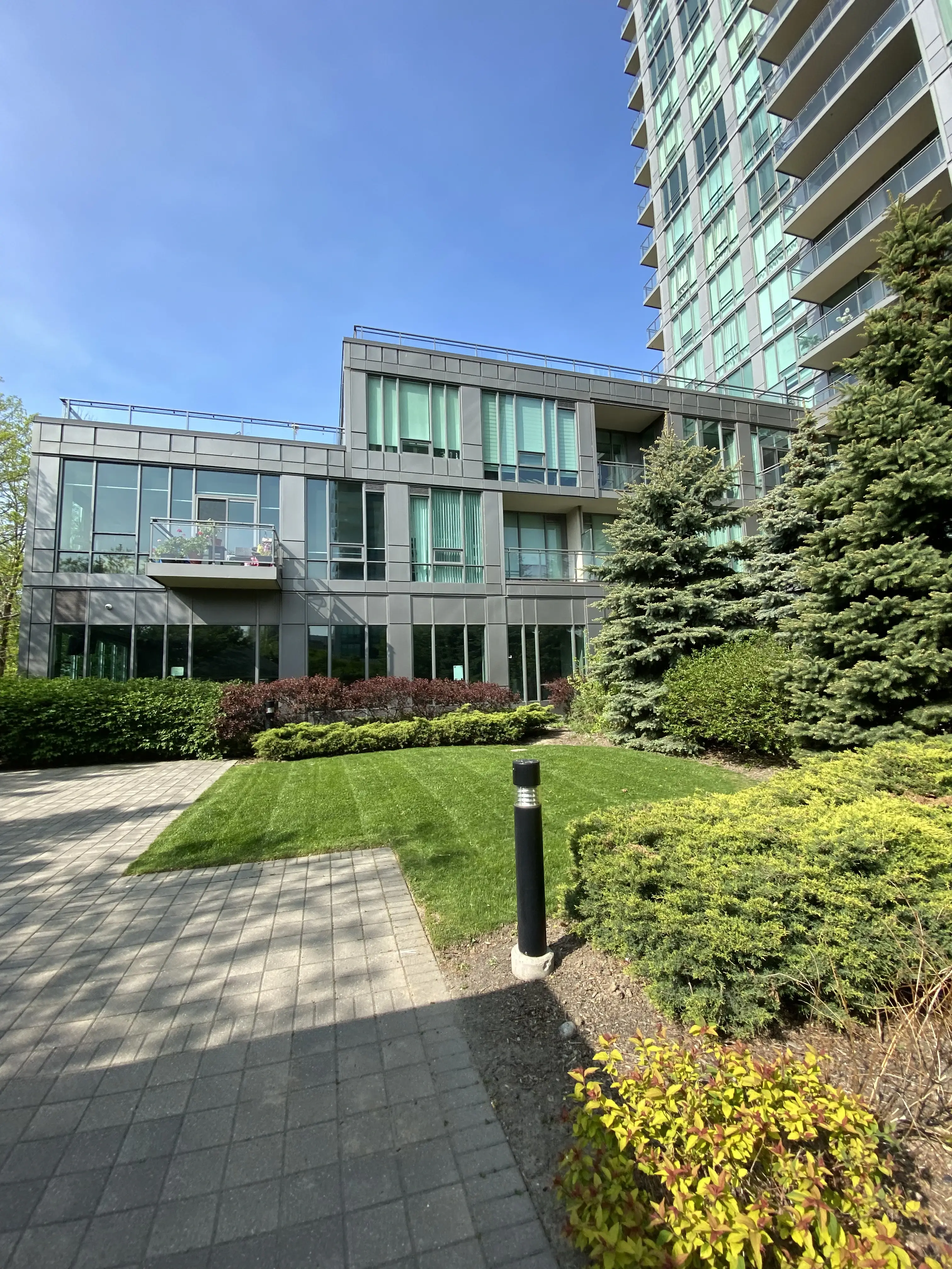 Lush green landscaping and evergreen trees in front of a high-rise glass building designed by Falcons Landscaping.