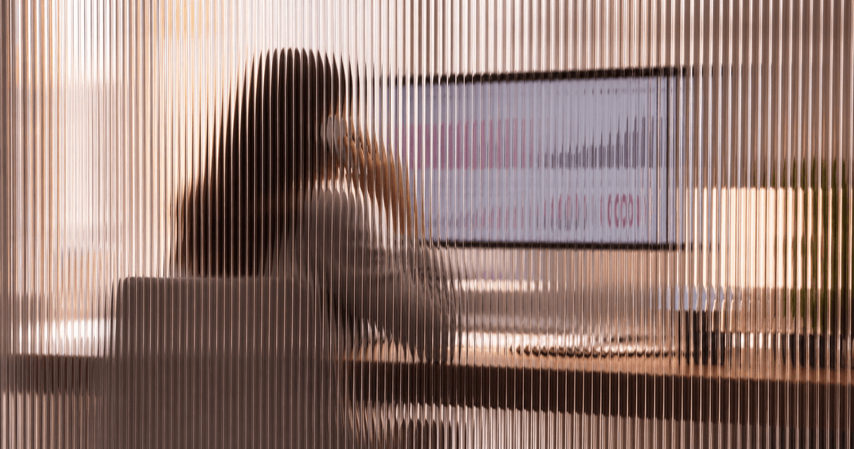 Marketer reviewing a campaign dashboard, phone in hand to call a lead, seen through vertical fluted glass