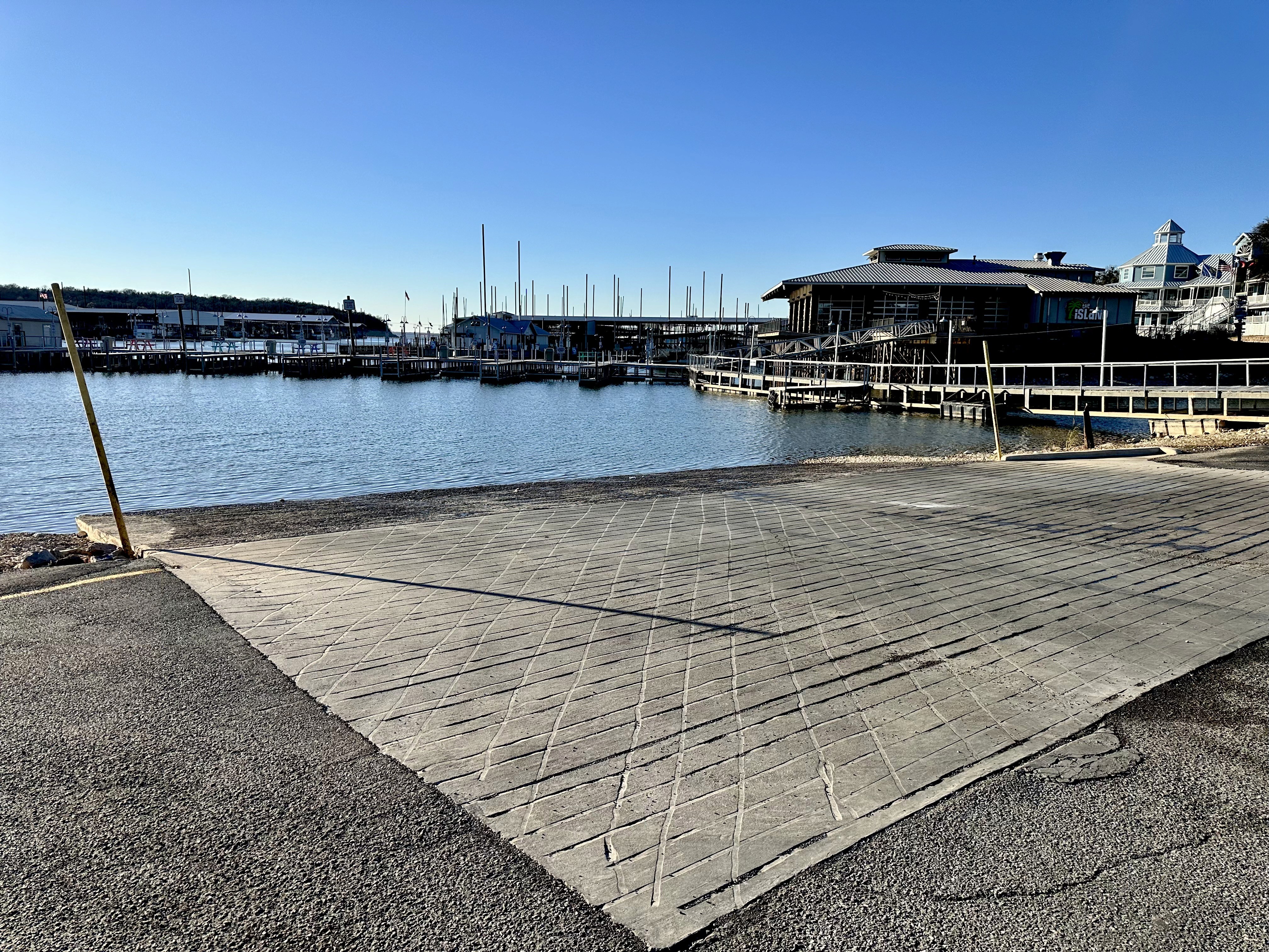 A boat ramp in the foreground leading to calm water and numerous moored sailboats in the background at highport marina in lake texoma in pottsboro tx.