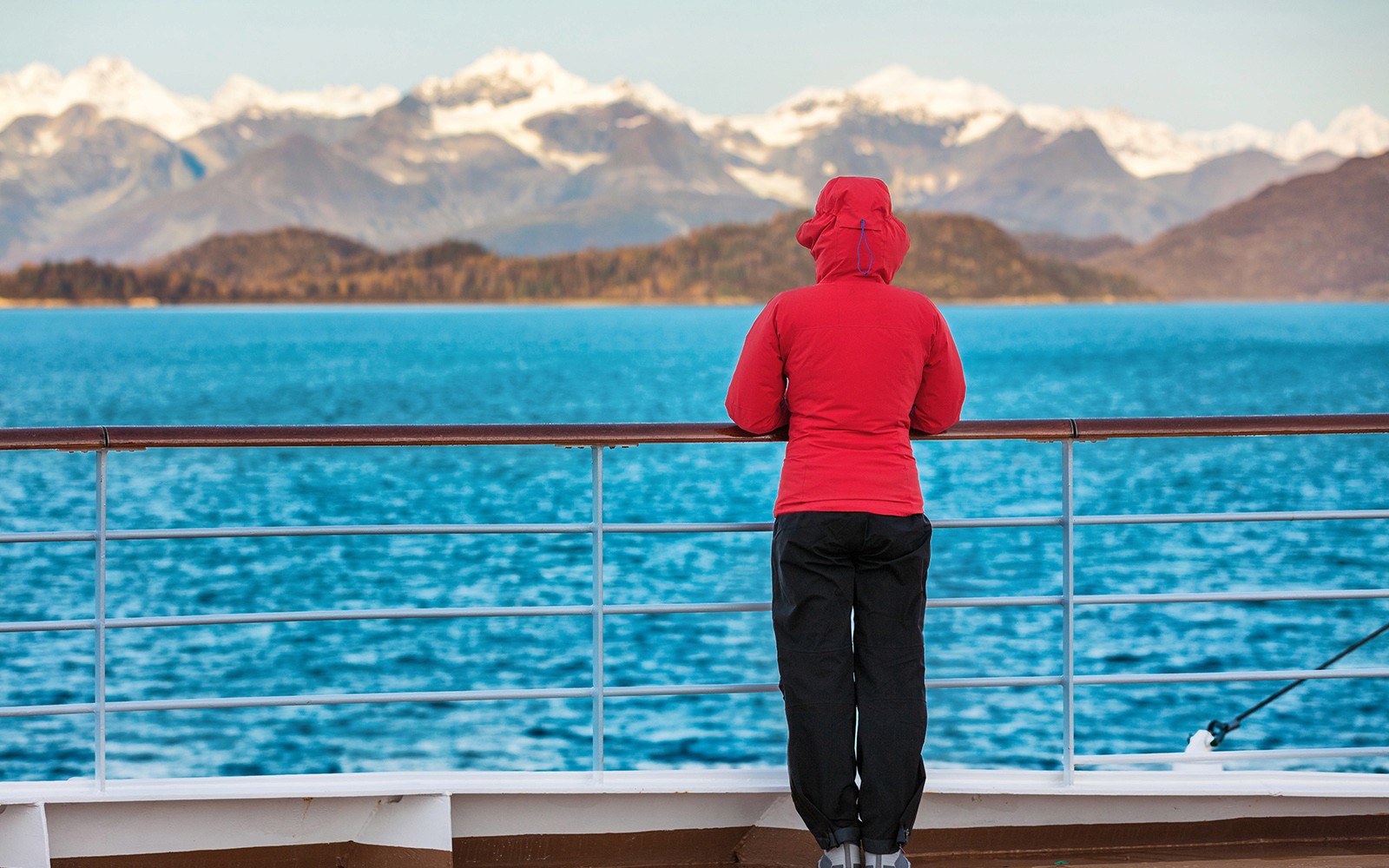 Personne en veste rouge sur le pont du navire de croisière avec vue sur les montagnes et le lac lors de la visite de Lugano et Bellagio.