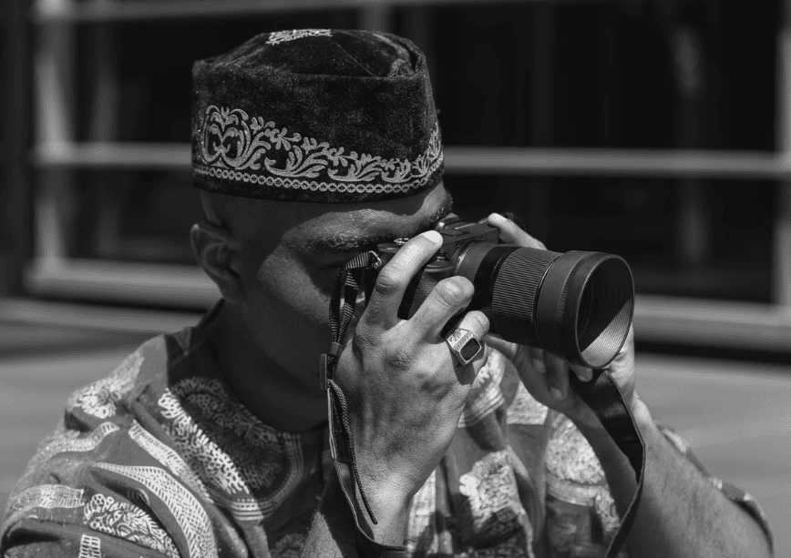 Man in traditional Nigerian attire taking a photo with a camera, symbolizing verified identity, digital focus, and authenticity through Profiled Nigeria.