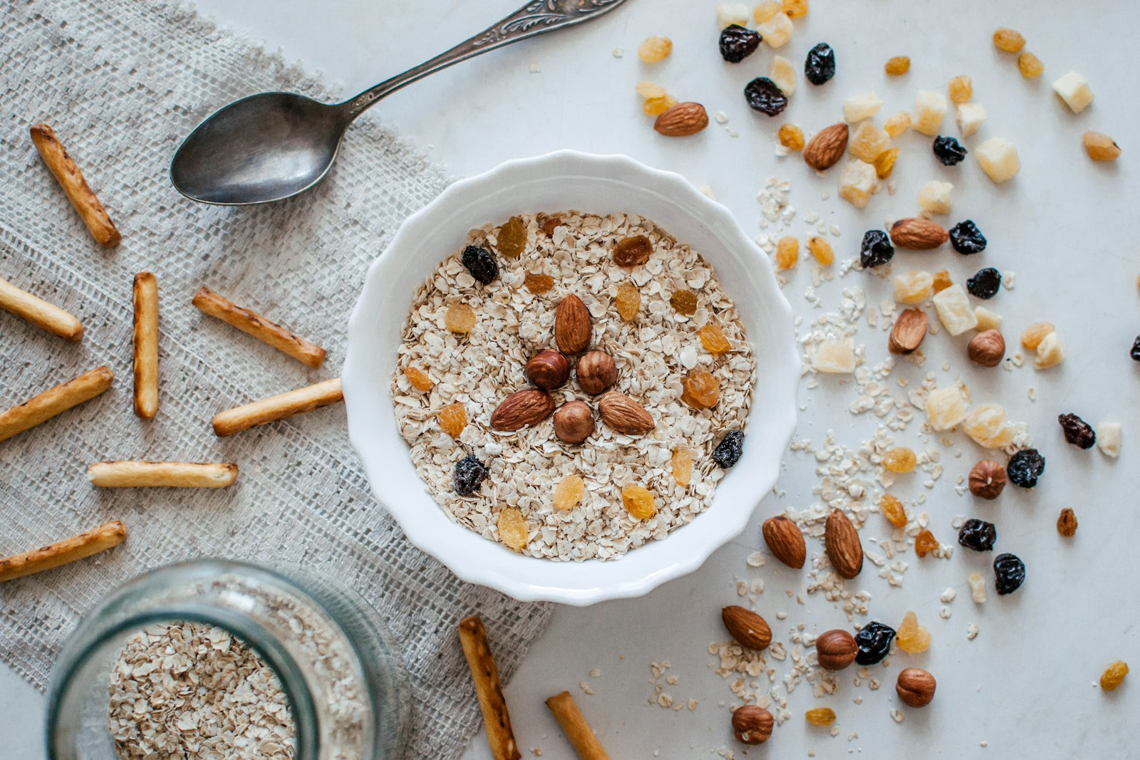 A bowl of oats topped with almonds and dried fruit surrounded by nuts, high-fiber foods that fuel beneficial gut bacteria