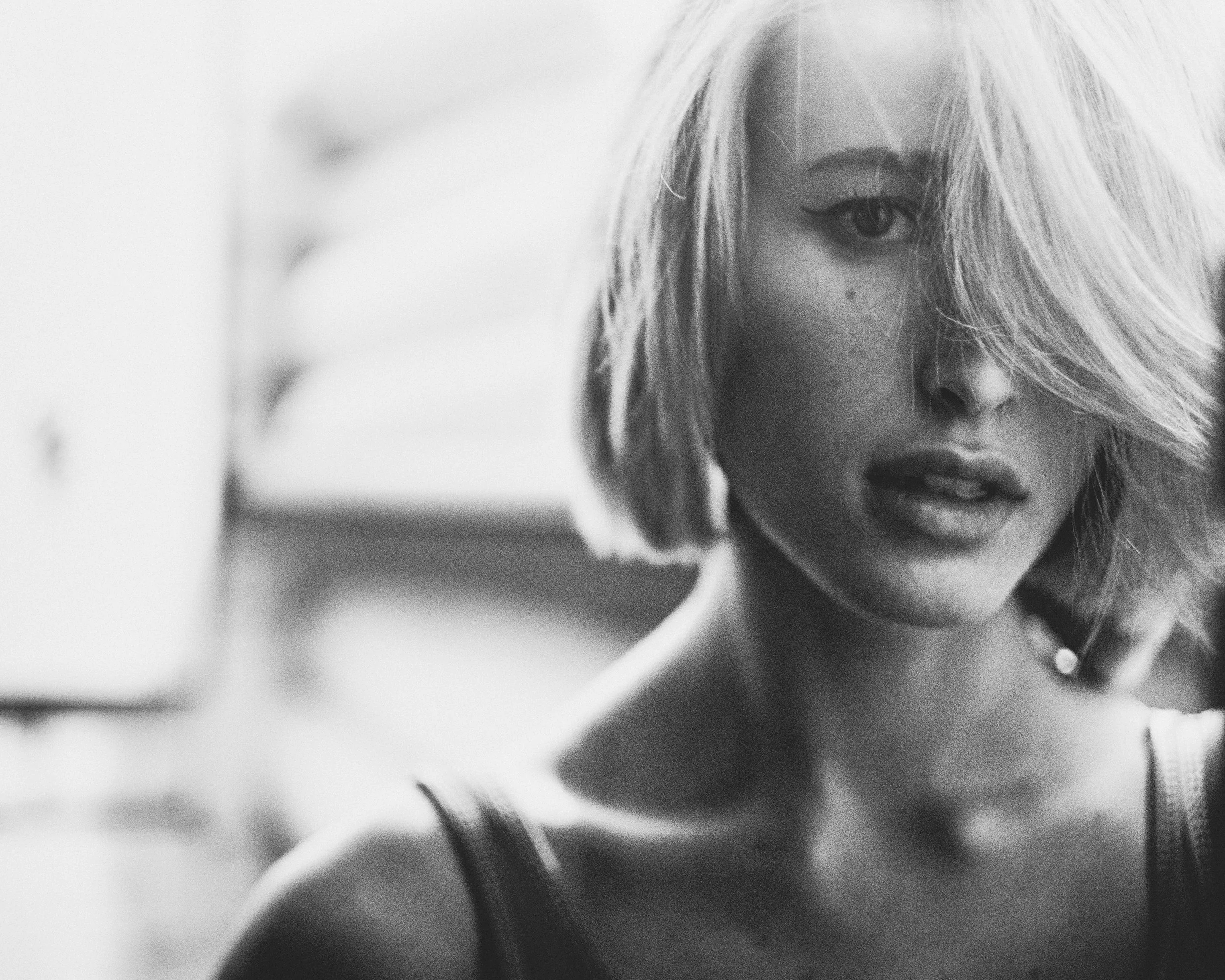 Black-and-white portrait of a blonde woman with a short bob, hair across her face, soft natural light.