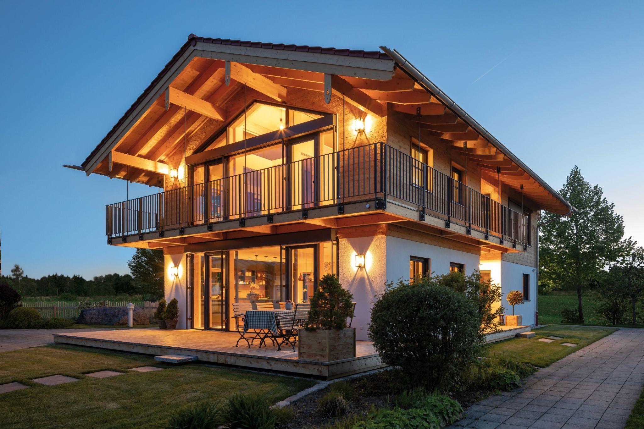 Modernes Holzhaus mit großem Balkon und Terrasse, beleuchtet bei Abenddämmerung.