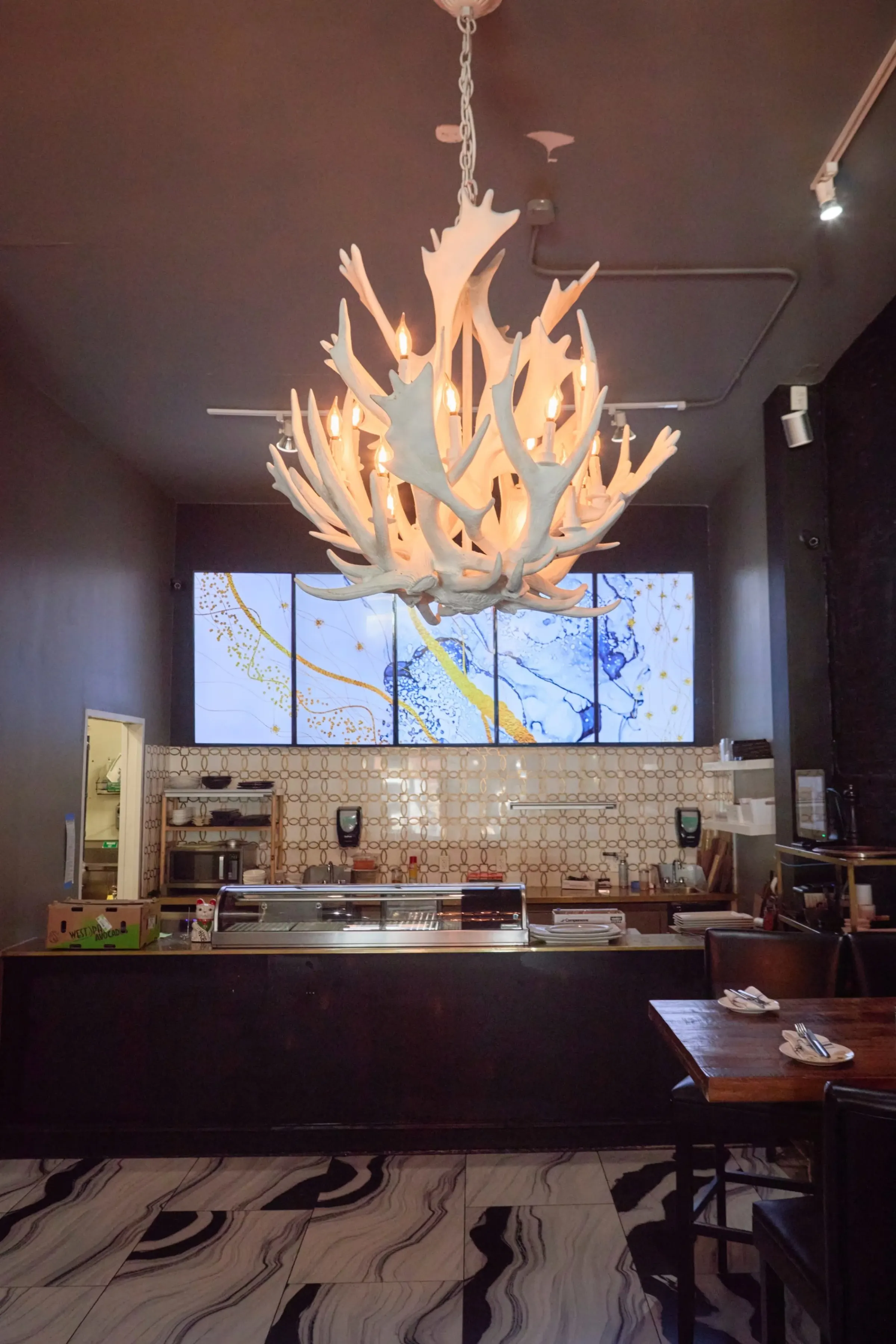 South Village Grille bar area with antler chandelier and art screens