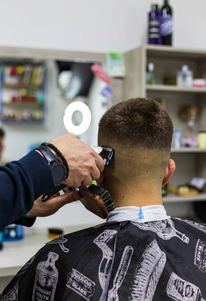 Buzz Cut at a Barbershop: A professional barber using electric clippers to give a clean, sharp buzz cut to a young man. The barbershop has a simple and clean interior, emphasizing efficiency and cleanliness.