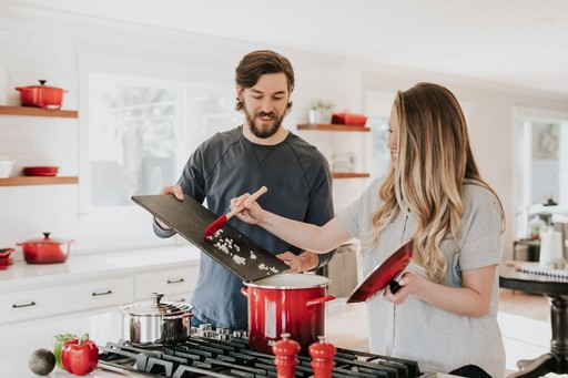 A man and a woman are interacting in a bright kitchen, surrounded by red kitchenware and engaging with each other.