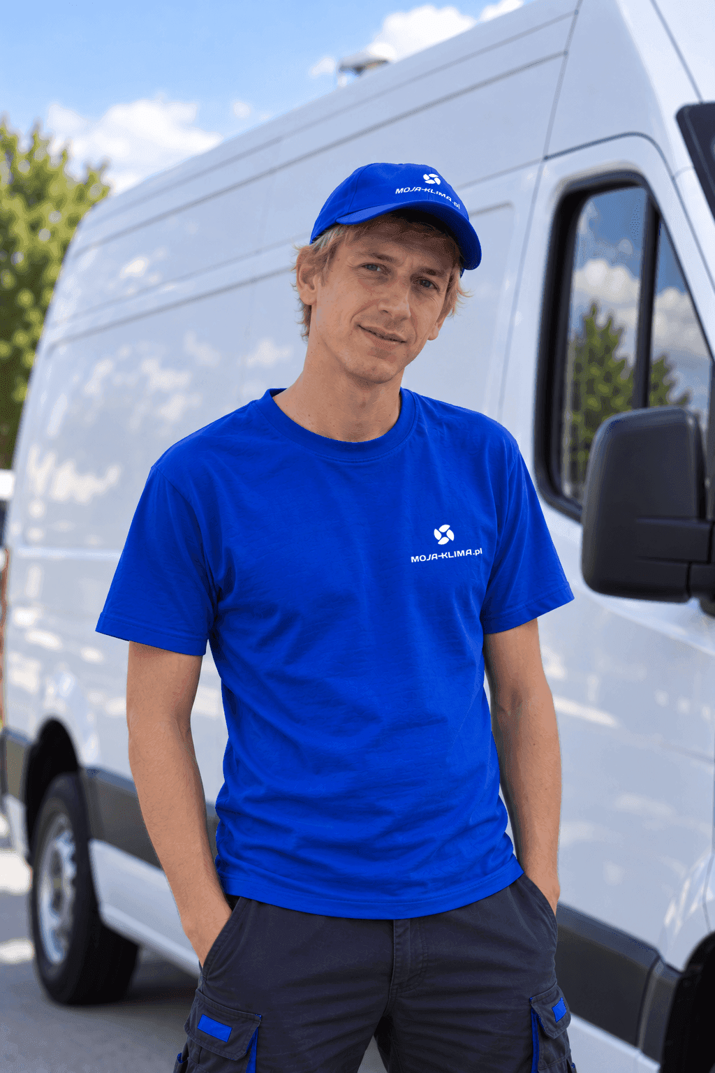 Artur - mężczyzna  23 lata w firmowej niebieskiej koszulce i czapce. Na tle samochodu dostawczego.  Montażysta moja-klima.pl