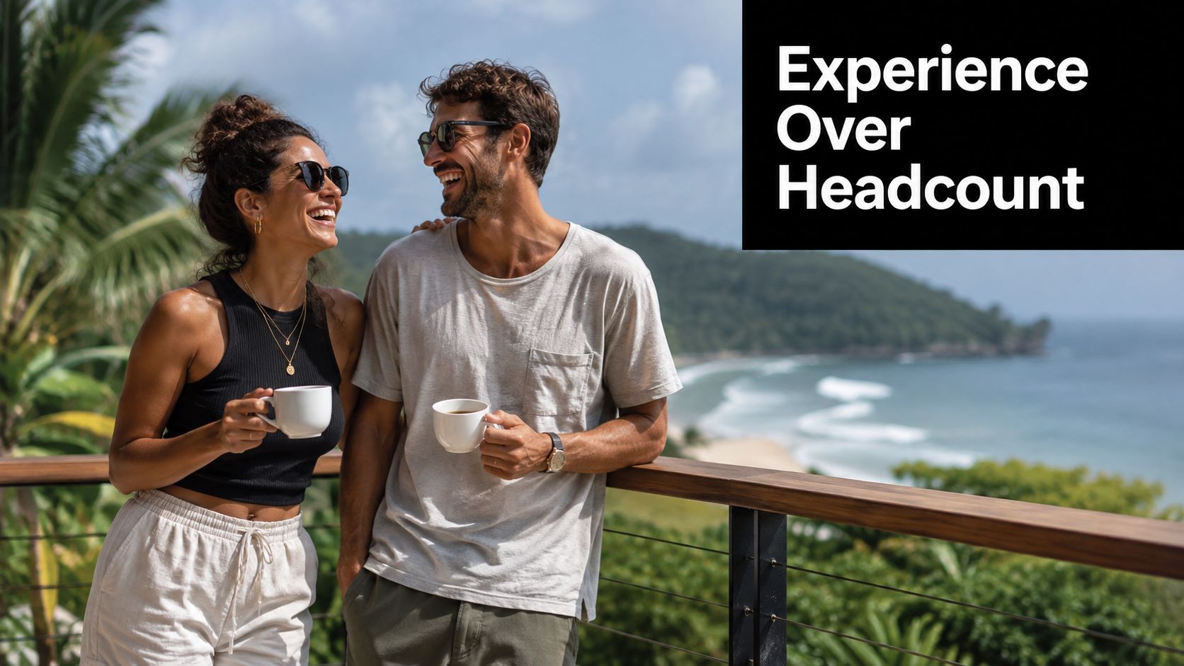 A happy couple enjoying coffee together on a balcony with a scenic ocean and mountain view.