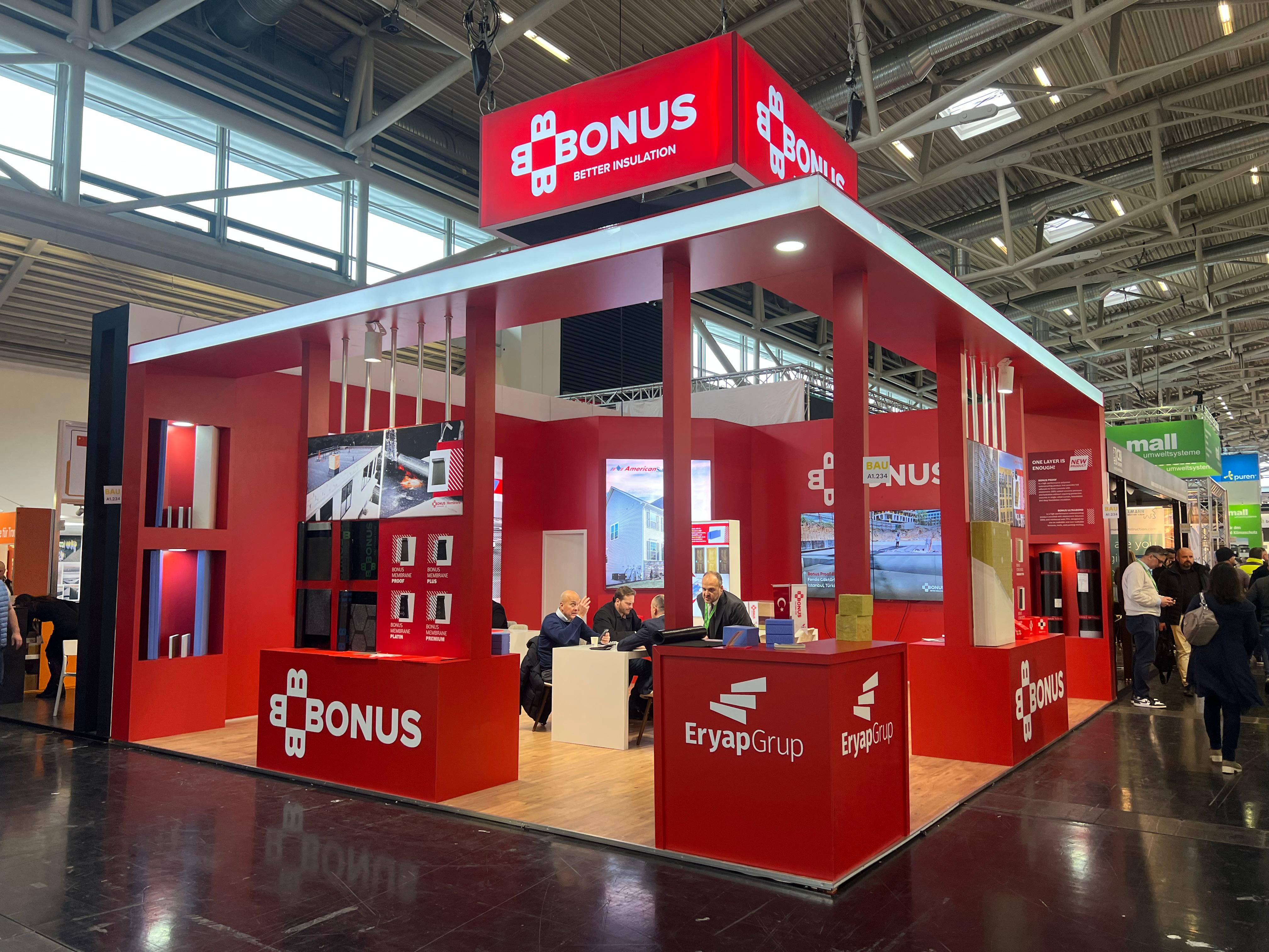 BONUS exhibition stand at BAU 2025 Munich, featuring a bold red corporate identity, large red architectural frames, and strong illuminated branding.