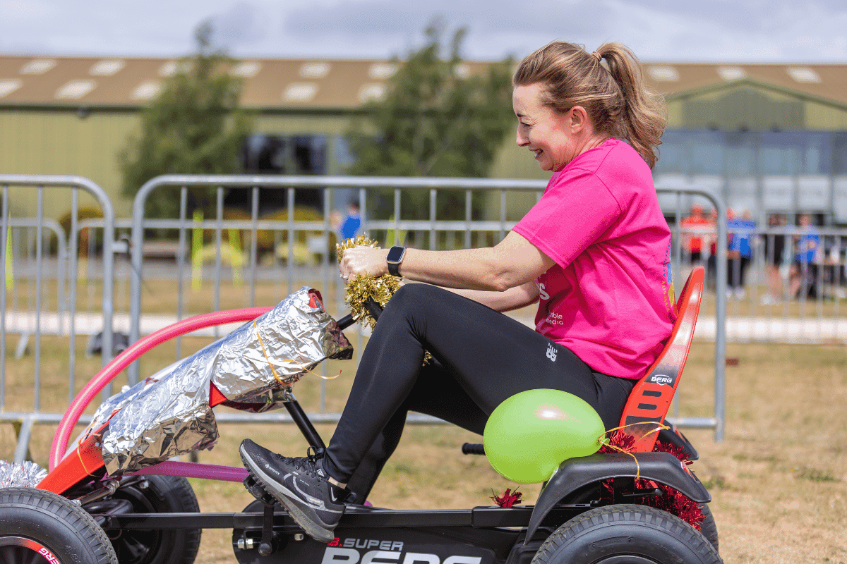 Outdoor team-building event with participants wearing matching blue shirts, taking part in inflatable obstacle courses and games, smiling and cheering, with the words 'ENTER A TEAM' in large bold white and green text across the image.