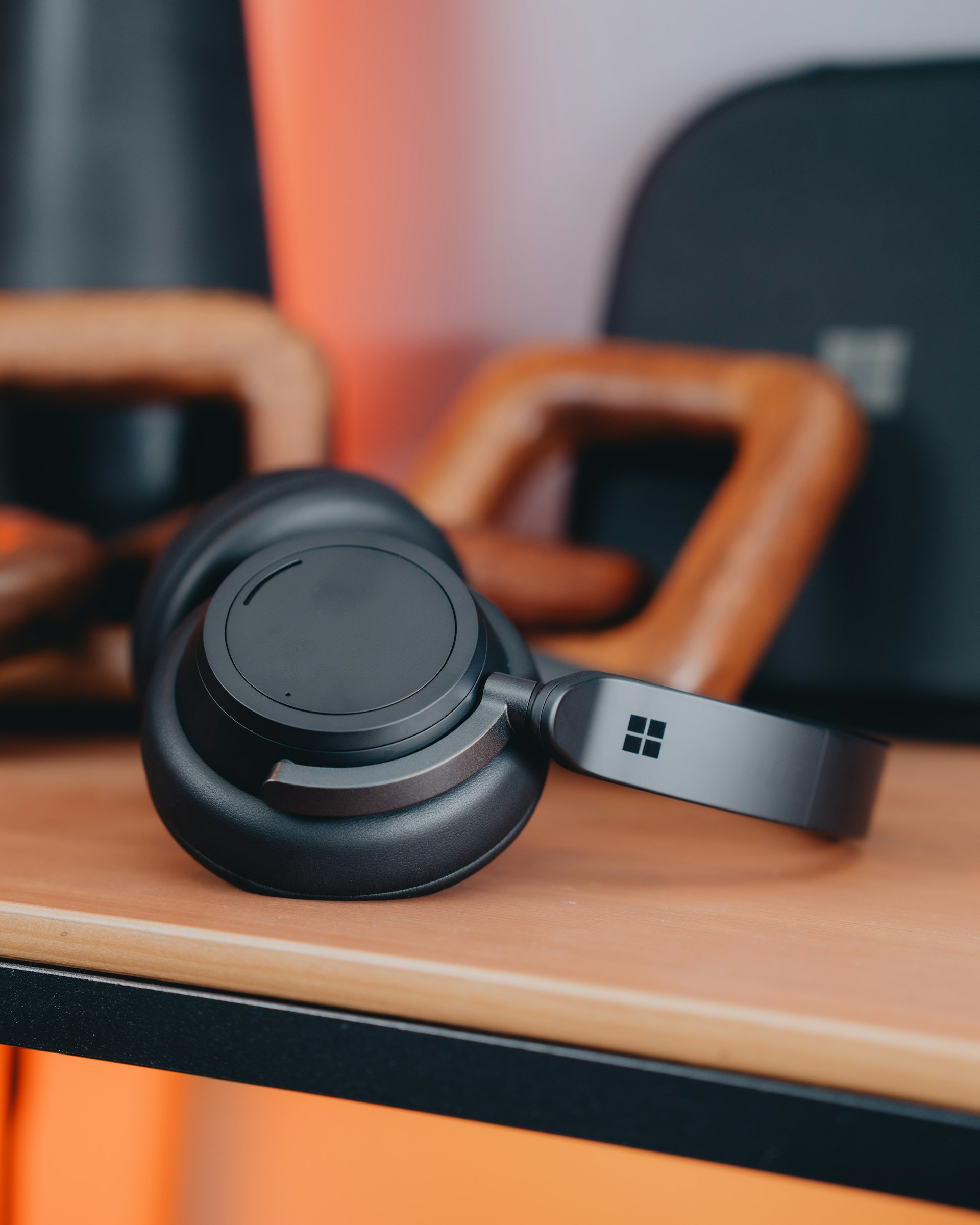 Close-up of black Microsoft Surface Headphones resting on a wooden shelf.