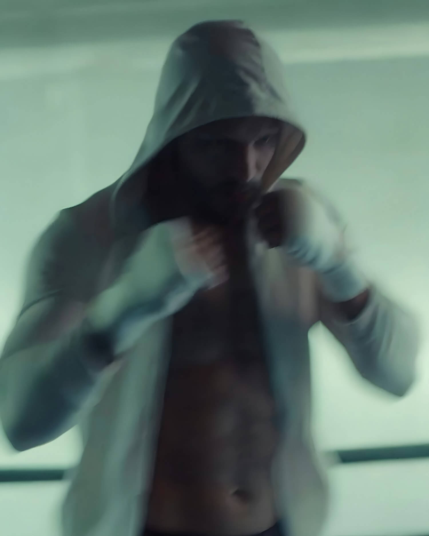 Man training indoors with boxing gloves and hood up