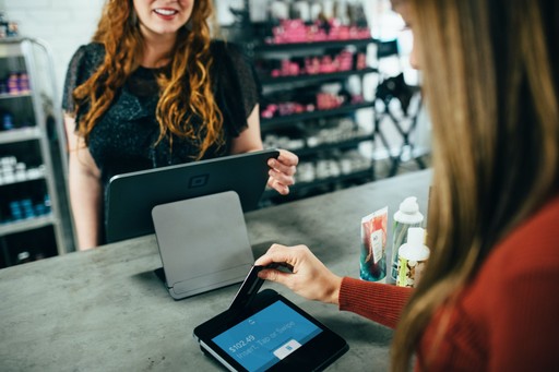 Customer paying with a card at a store counter while a clerk uses a tablet.
