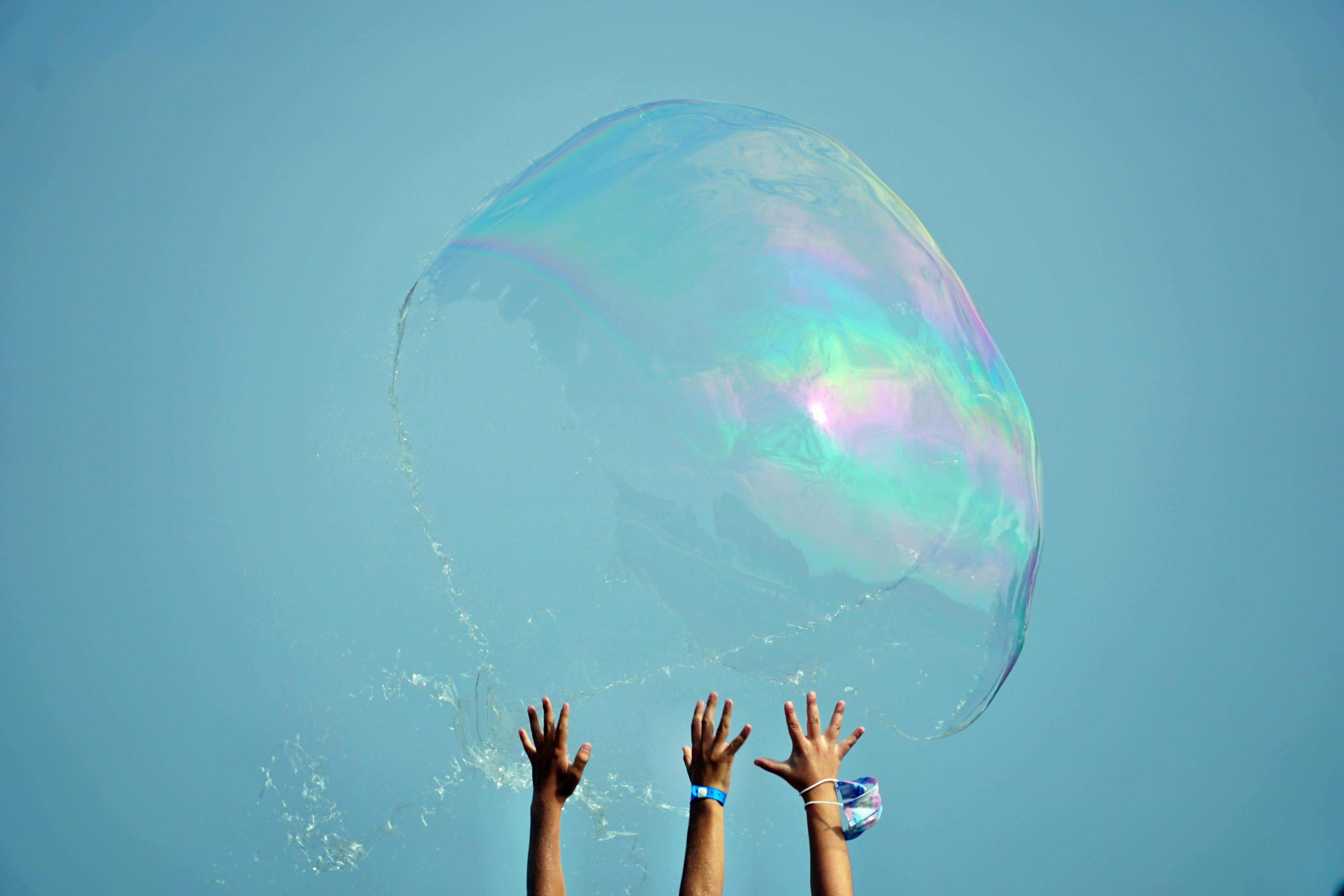 verschiedene Hände greifen nach einer großen Seifenblase vor blauem Himmel  - Foto von Pexels - Bernd von Darl