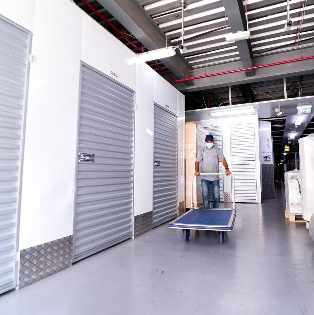 Modern business storage facility in Dubai, featuring labeled units and a flatbed cart in use by a masked worker.
