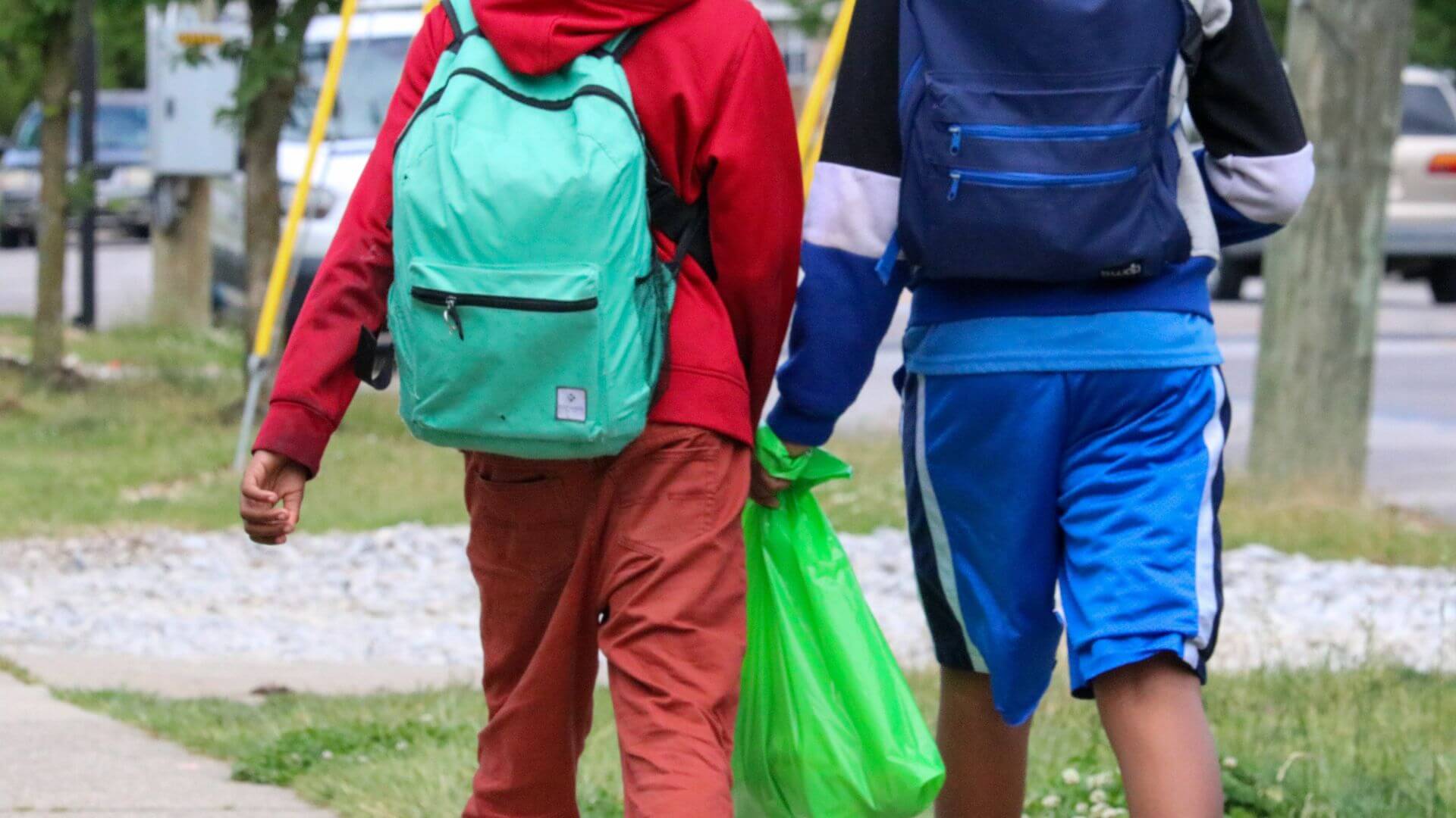 Four smiling children hold green food bags outside a building, showing joy after receiving meals.