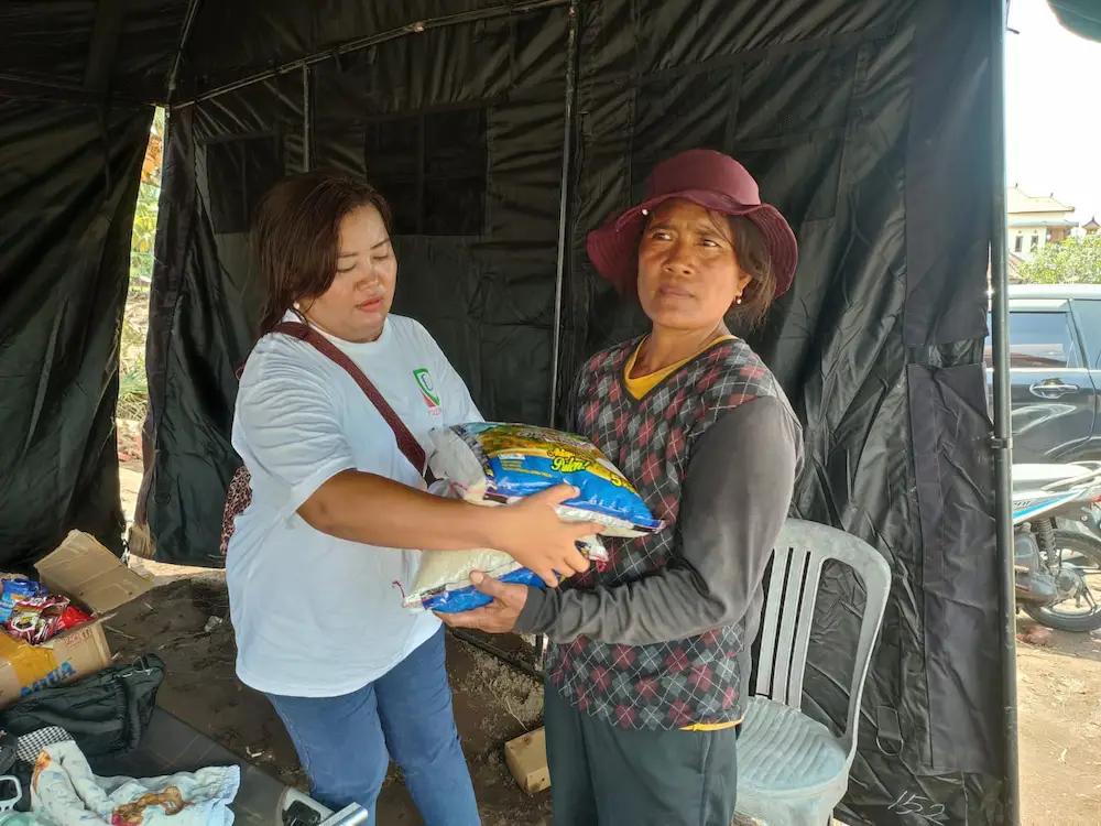 Volunteer delivers emergency food aid to a local woman at a disaster relief distribution point in Bali.