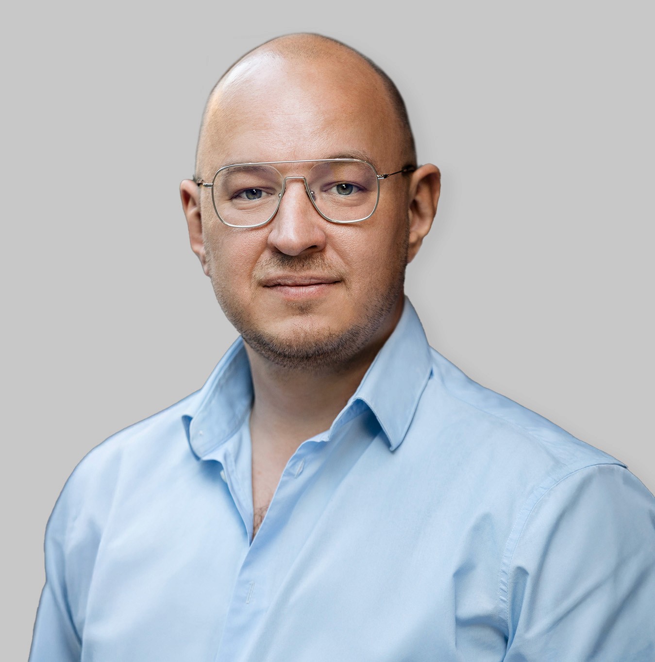Minimal studio portrait of a confident woman in a white shirt, arms crossed, on a soft gray background.