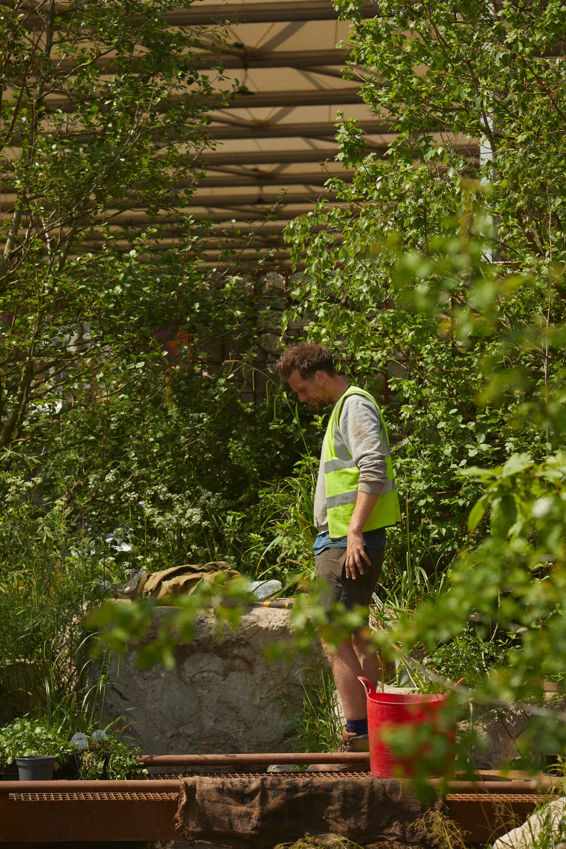 A person wearing a bright shirt stands near a water feature surrounded by lush greenery. 