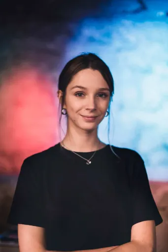 Portrait of person in black shirt with necklace against red and blue gradient background.