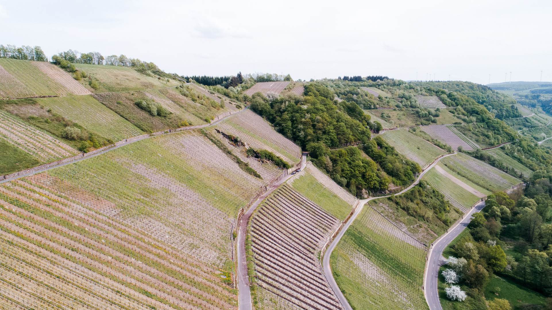An aerial view of rolling hills with winding roads and patches of greenery under a cloudy sky.