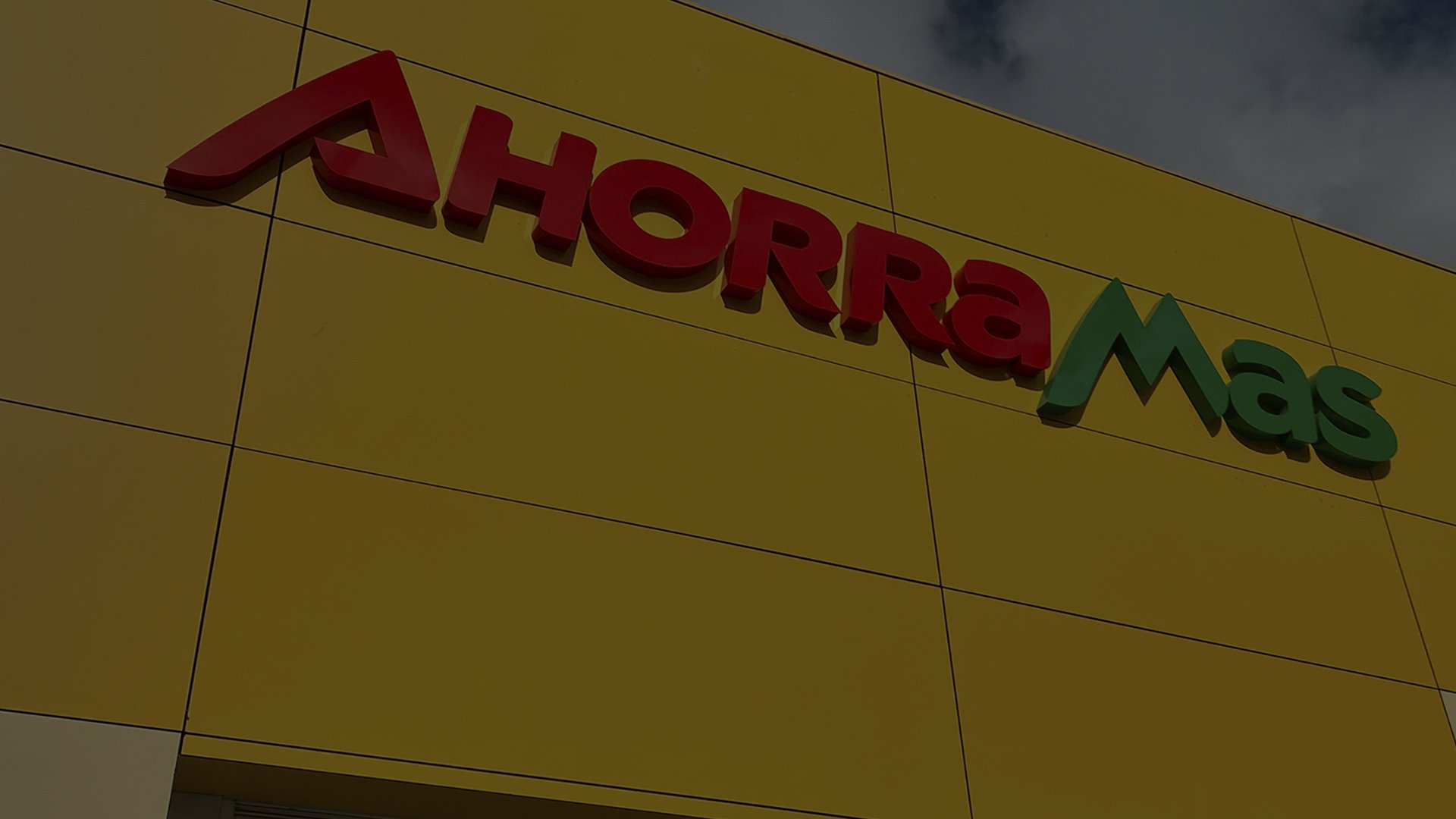 Yellow building facade with bold red and green "Ahorramas" sign. The bright colors convey a welcoming, vibrant tone against a cloudy sky.