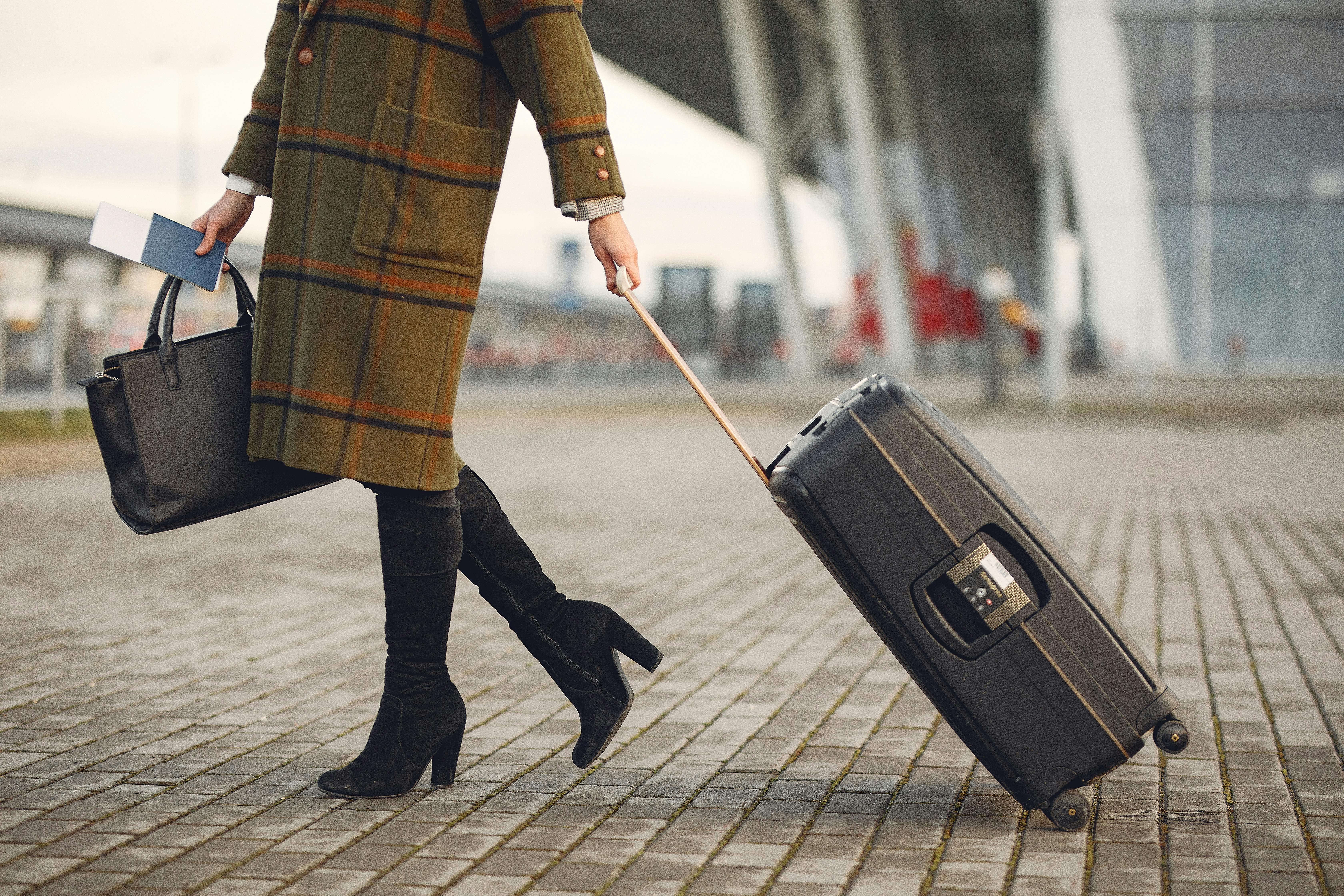 Person pulling a suitcase while walking through an airport with a travel bag and passport