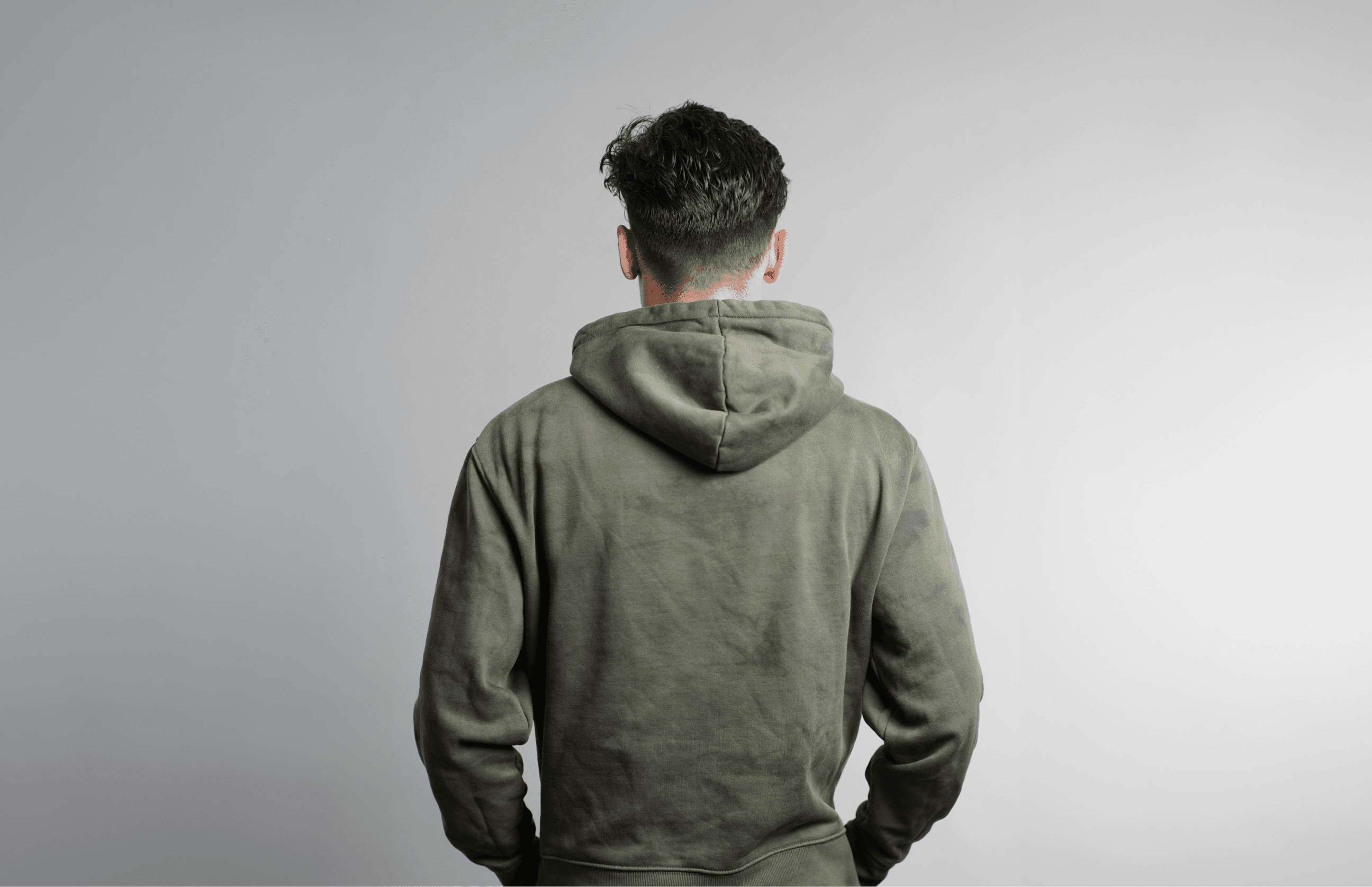 A portrait of Adam Sinda, a product designer, seated and looking thoughtfully off to the side. He is in a casual pose with his hands clasped, wearing a dark polo shirt. The background is a warm, neutral tone, and his name is repeated in large white letters, emphasizing his personal brand. Below his name, text states his occupation and his current position at Whatnot.