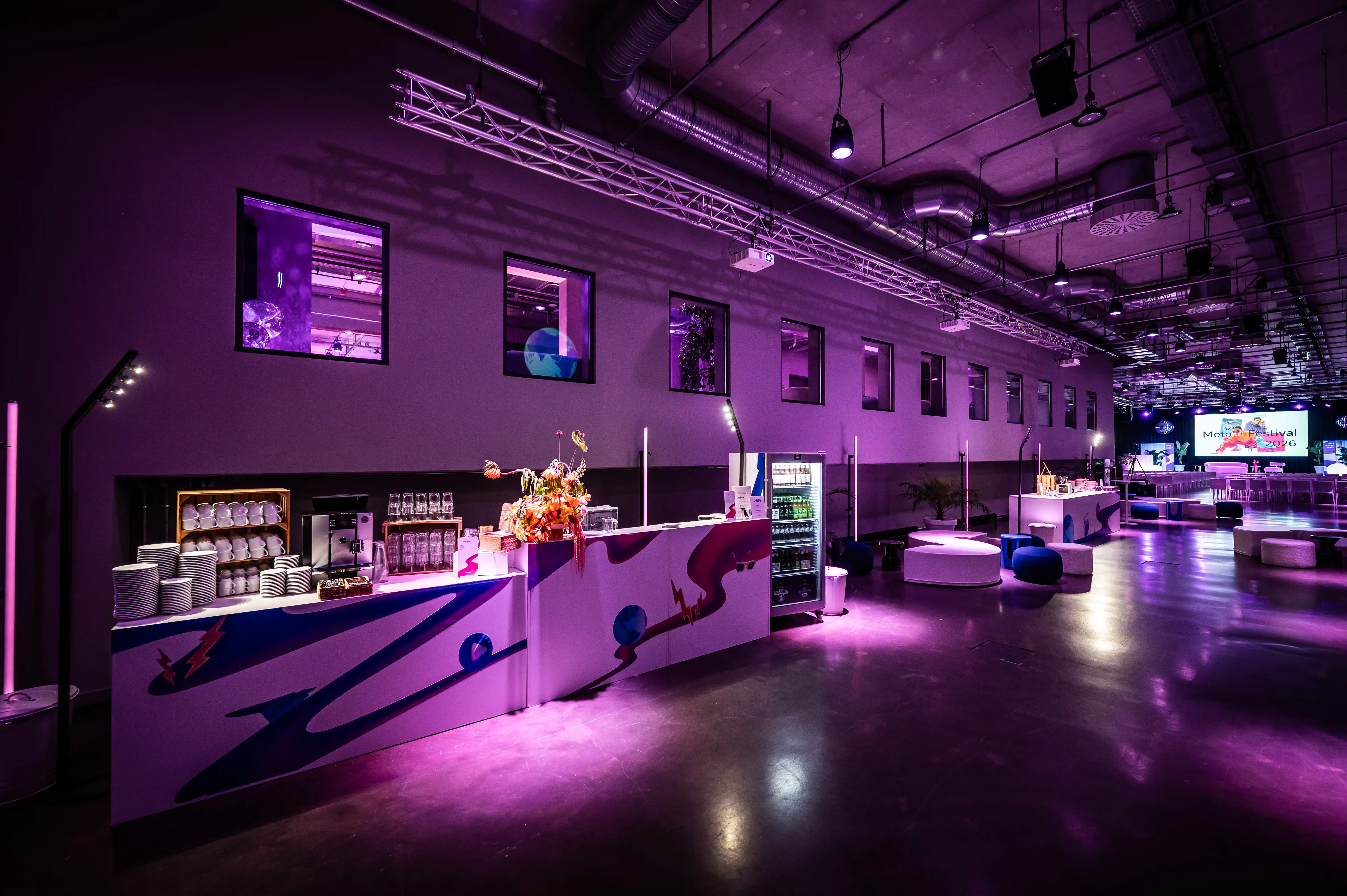 Purple-lit bar counters with colourful graphics, flowers and coffee station at the Meta Festival.