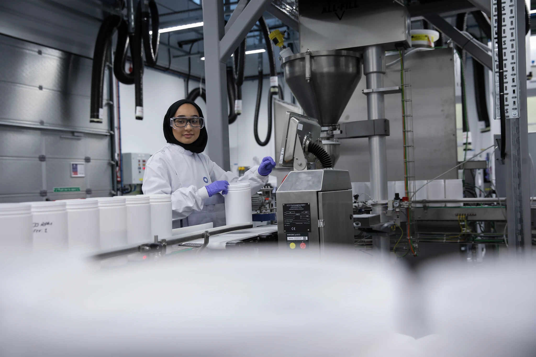 CPI scientist operating an automated powder filling line, handling white tubs on the conveyor.