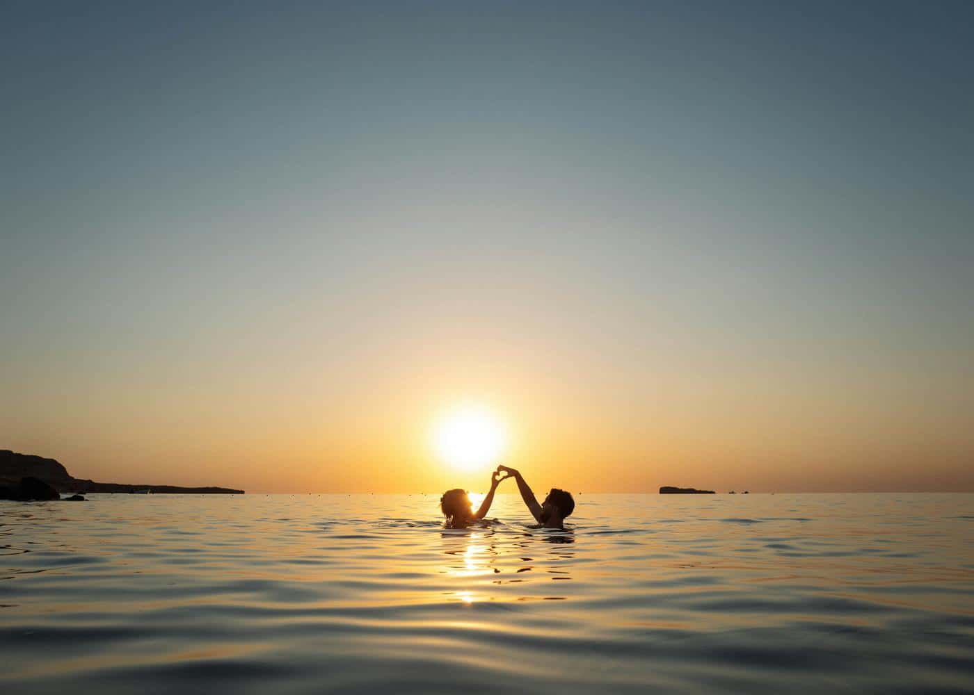 Two people swimming and forming a heart with their hands