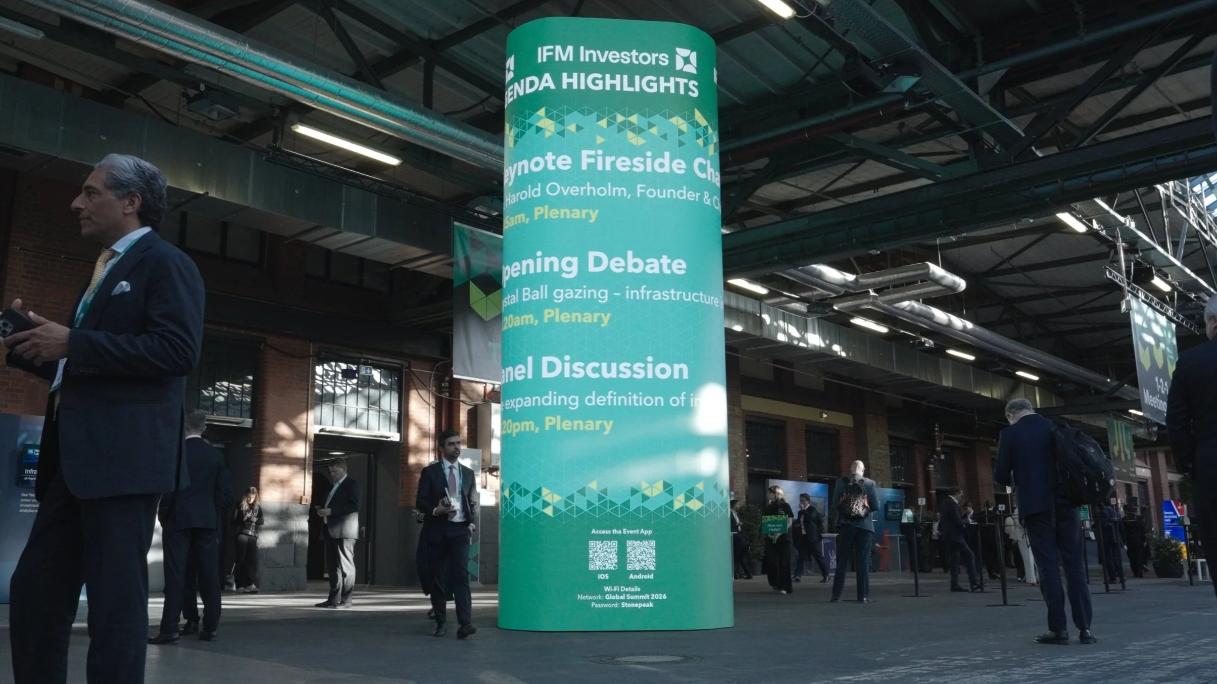 Delegates beside a tall green digital agenda display in the conference hall at STATION Berlin.