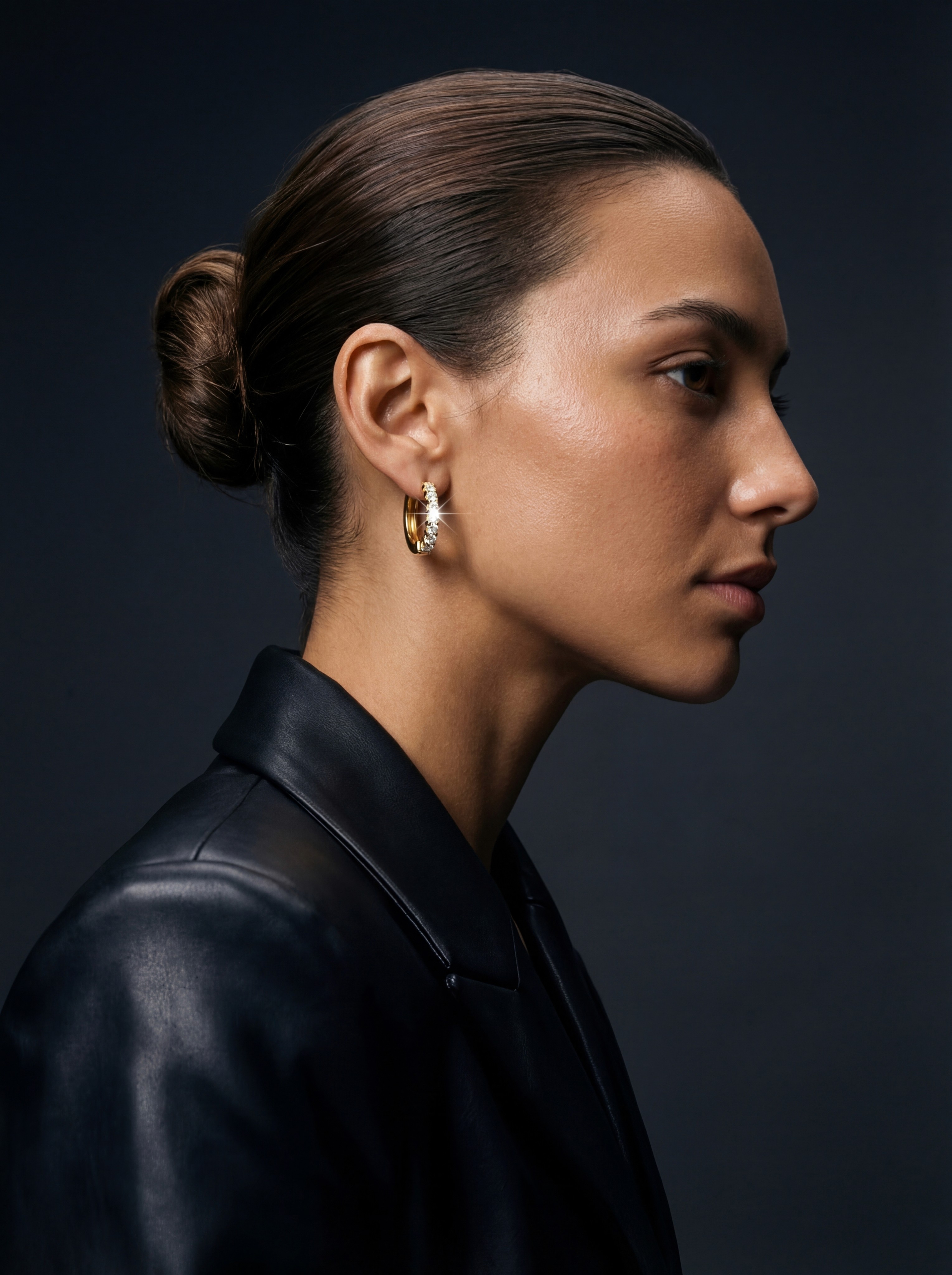 Side profile of a woman wearing gold earrings with dramatic lighting