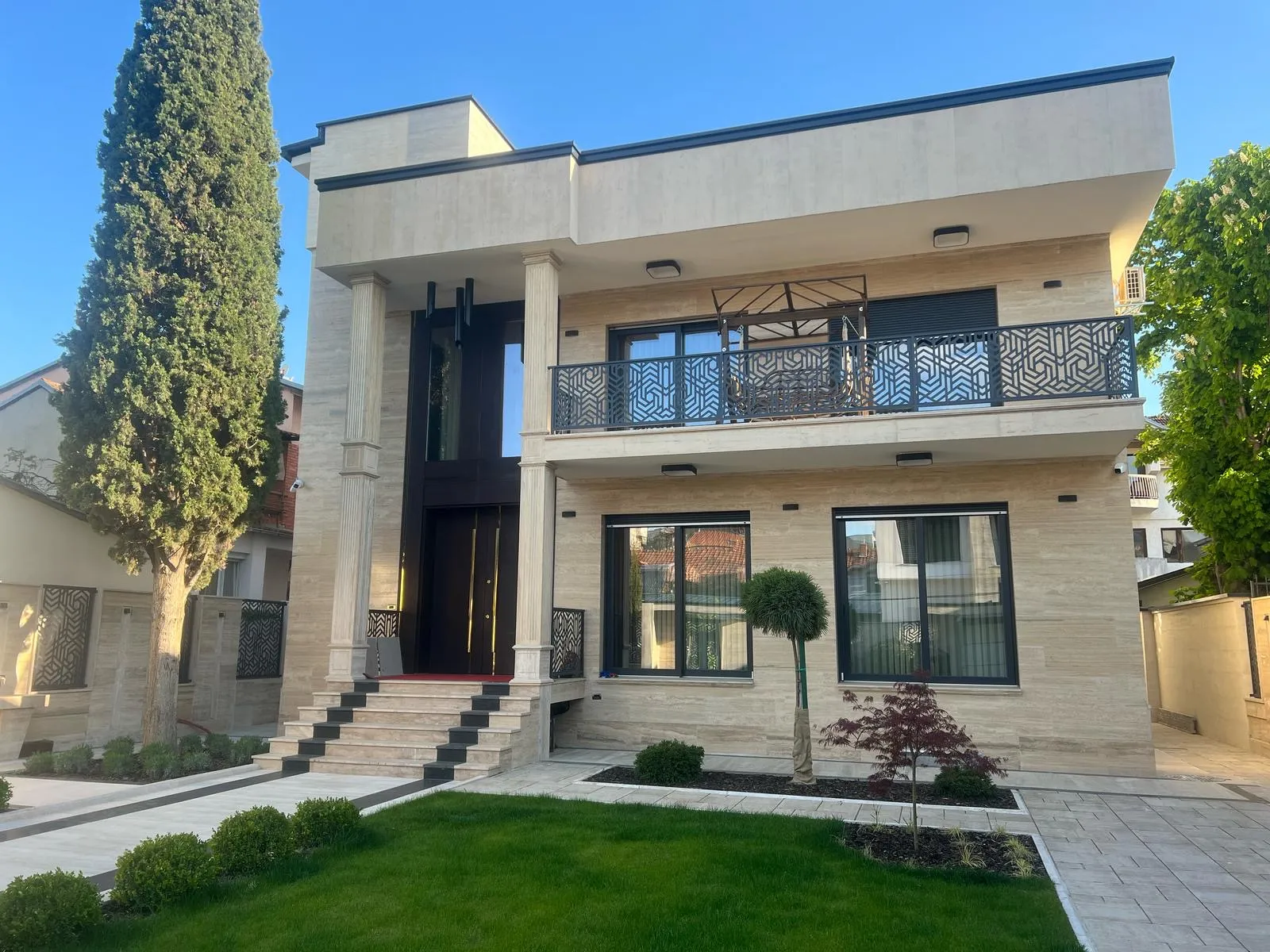 Modern private residence in Skopje with stone cladding, tall columns, and landscaped front garden. Terraplan Partners provided architectural planning and supervision.