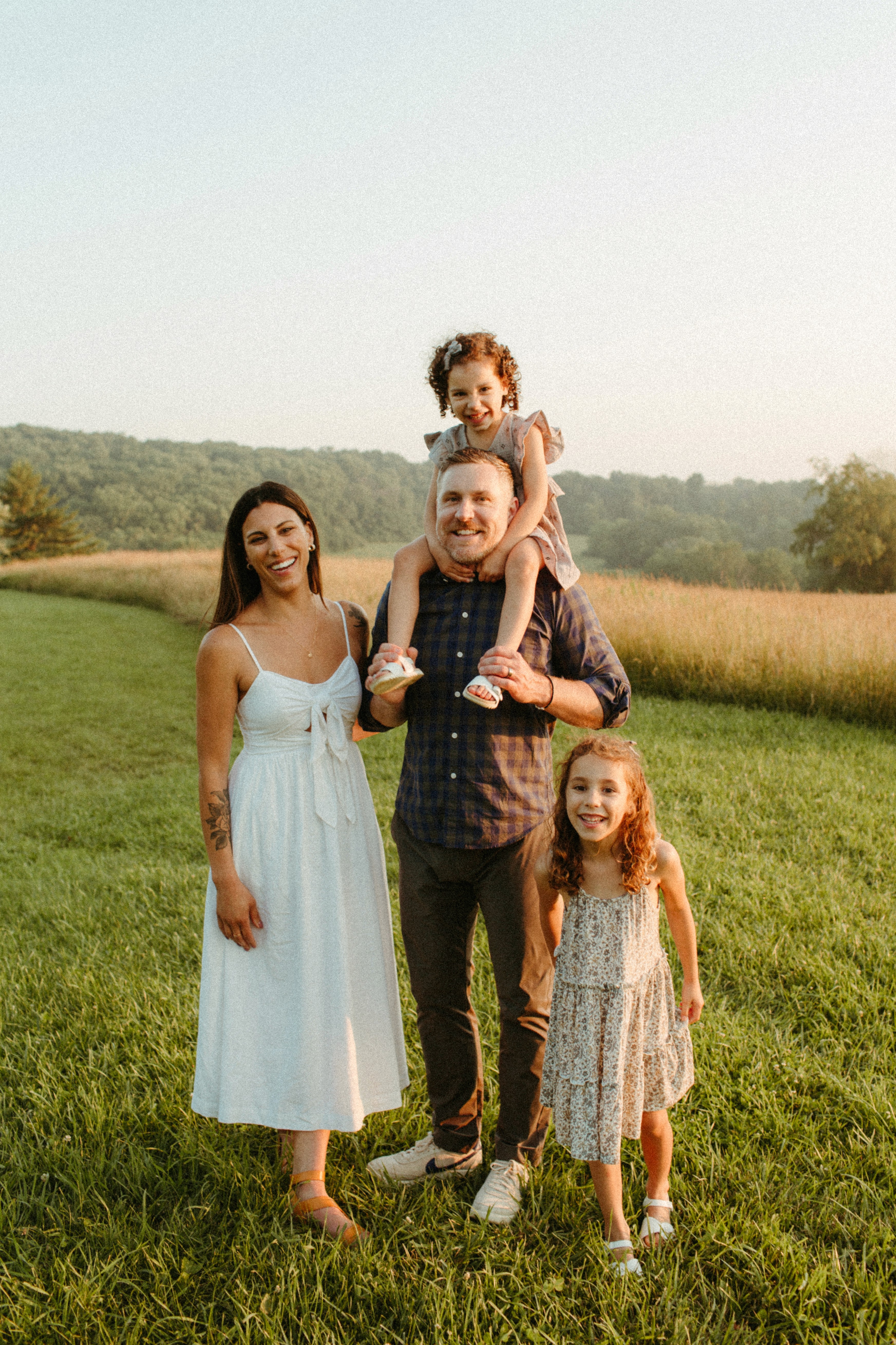 A woman in a white blouse and dark vest sits on a park bench, looking away and smiling. A ukulele rests next to her.