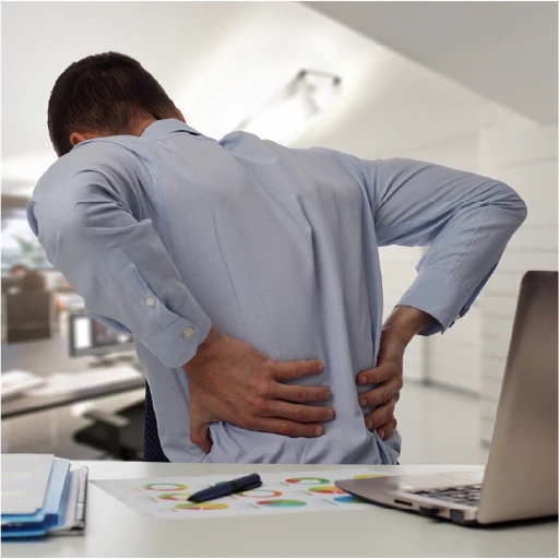 Man in an office setting holding his lower back, experiencing back pain often caused by prolonged sitting and poor posture at work