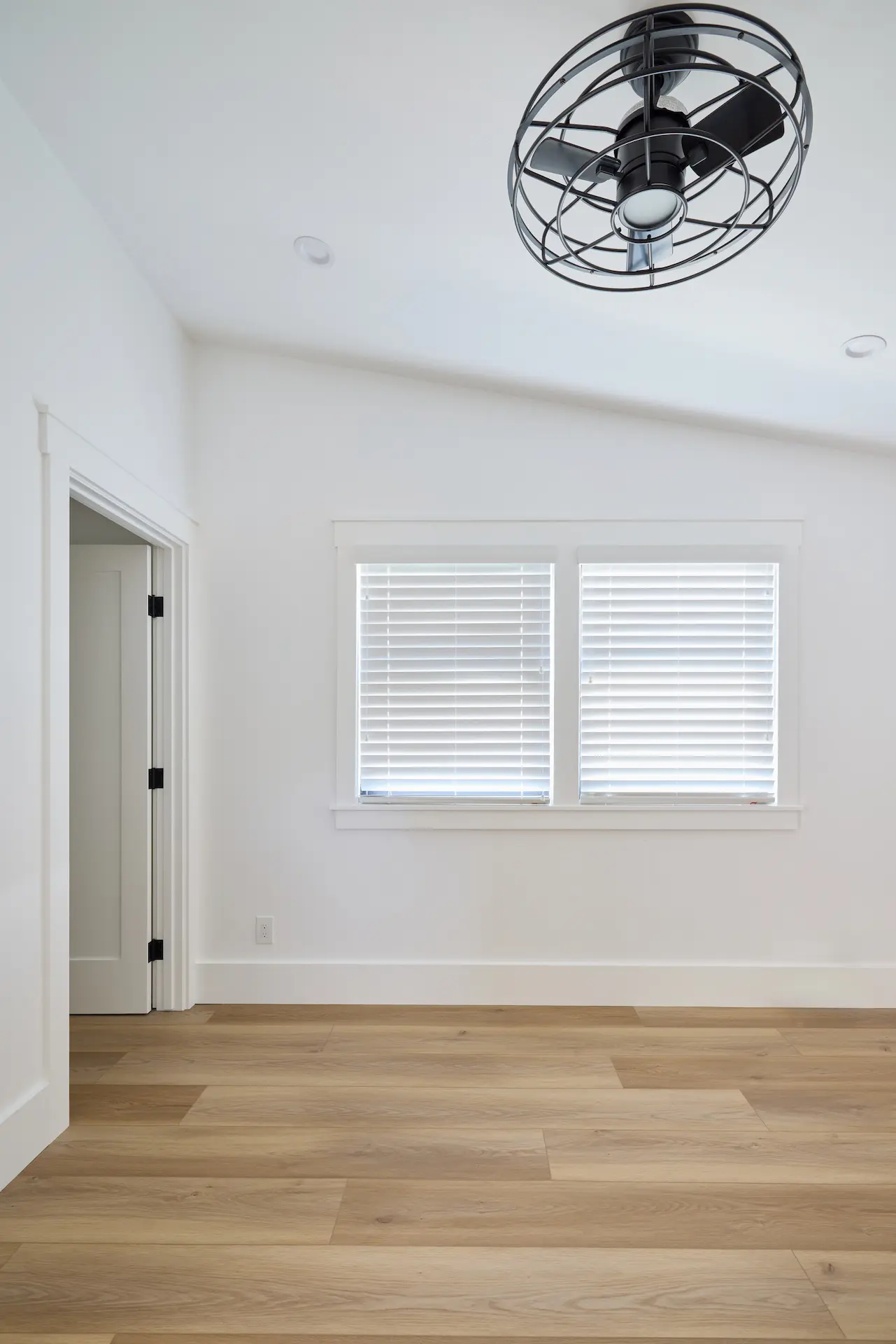 Portrait of the bedroom in ADU Orange, featuring Craftsman-style baseboards and window casings, vinyl flooring, with a modern ceiling fan above. Photo by Todd Huge.