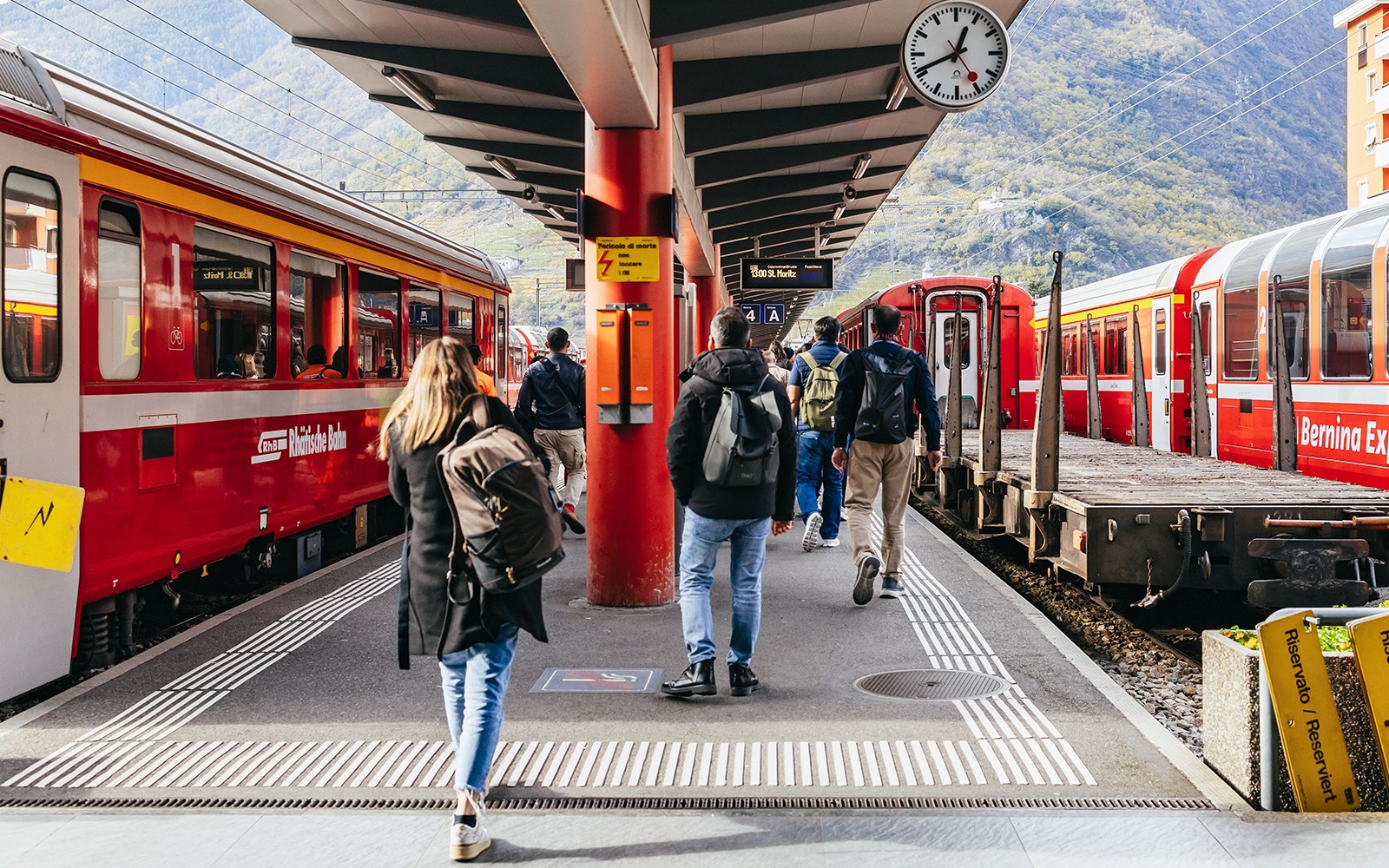 מטיילים העולים על רכבת ברנינה האדומה בתחנה בסנט מוריץ, מוקפים בהרים.