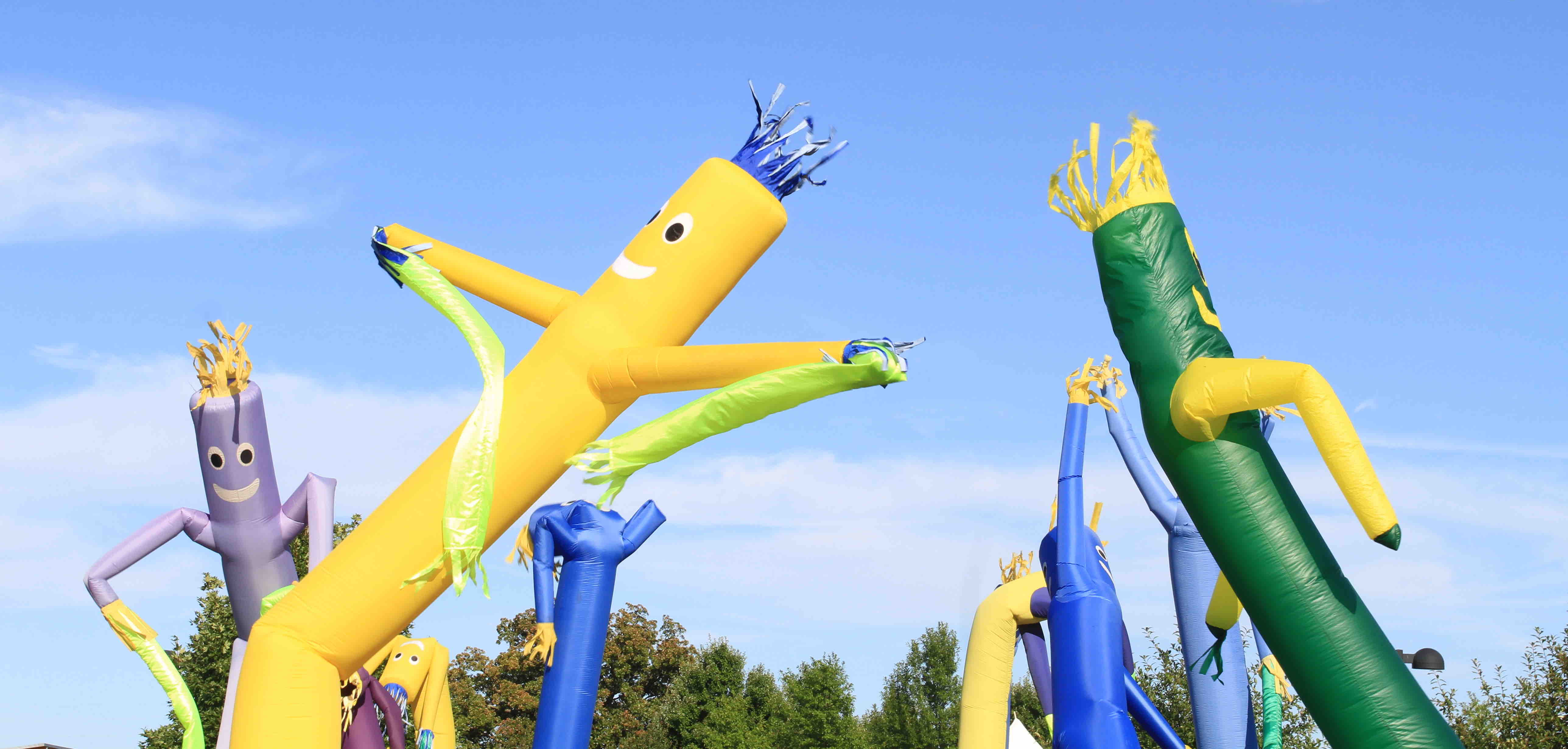 Colorful inflatable tube figures sway in the wind against a clear blue sky.