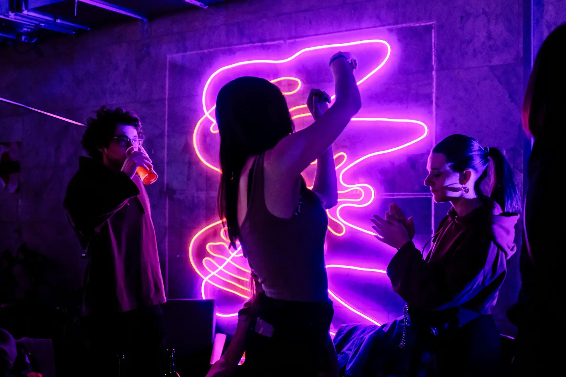 Guests dancing and enjoying drinks under neon lights during a themed night event at a modern bar.