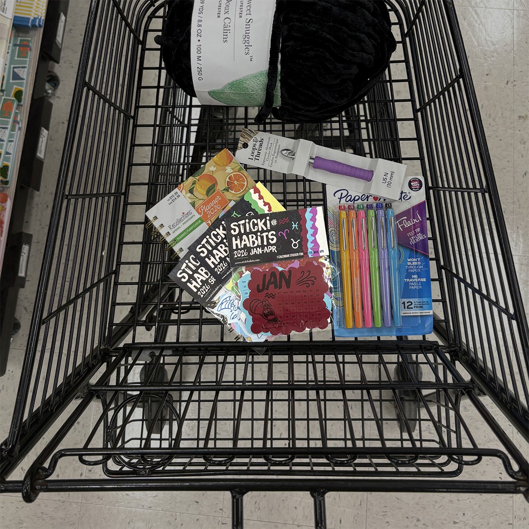 A top-down view of a shopping cart showing colorful stationery items and several “Sticki Habits” calendar sticker packs arranged flat inside the cart.