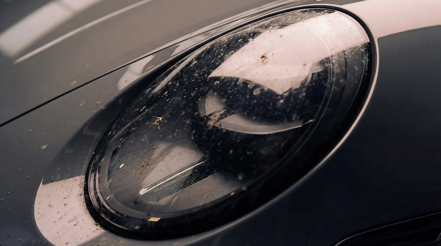 Avant nettoyage du phare avant d’une Porsche 911 avec traces et dépôts