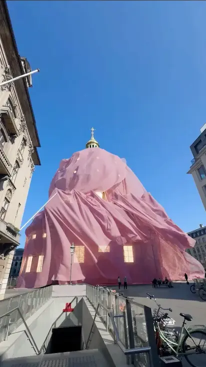 A massive, semi-transparent pink fabric drapes over a historic domed building in a surreal mixed-reality city scene