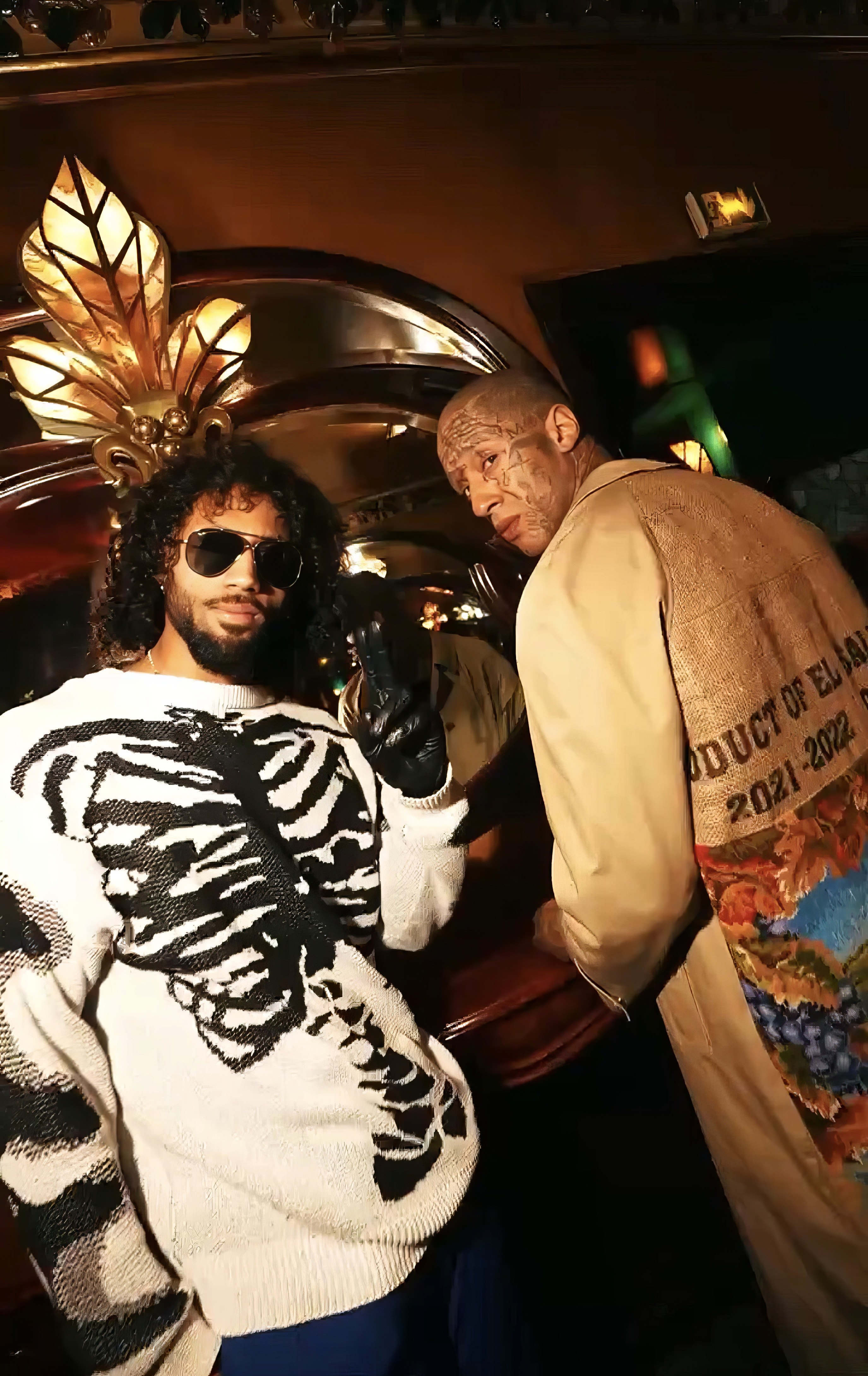 Bride sitting on ground against wall, groom standing nearby