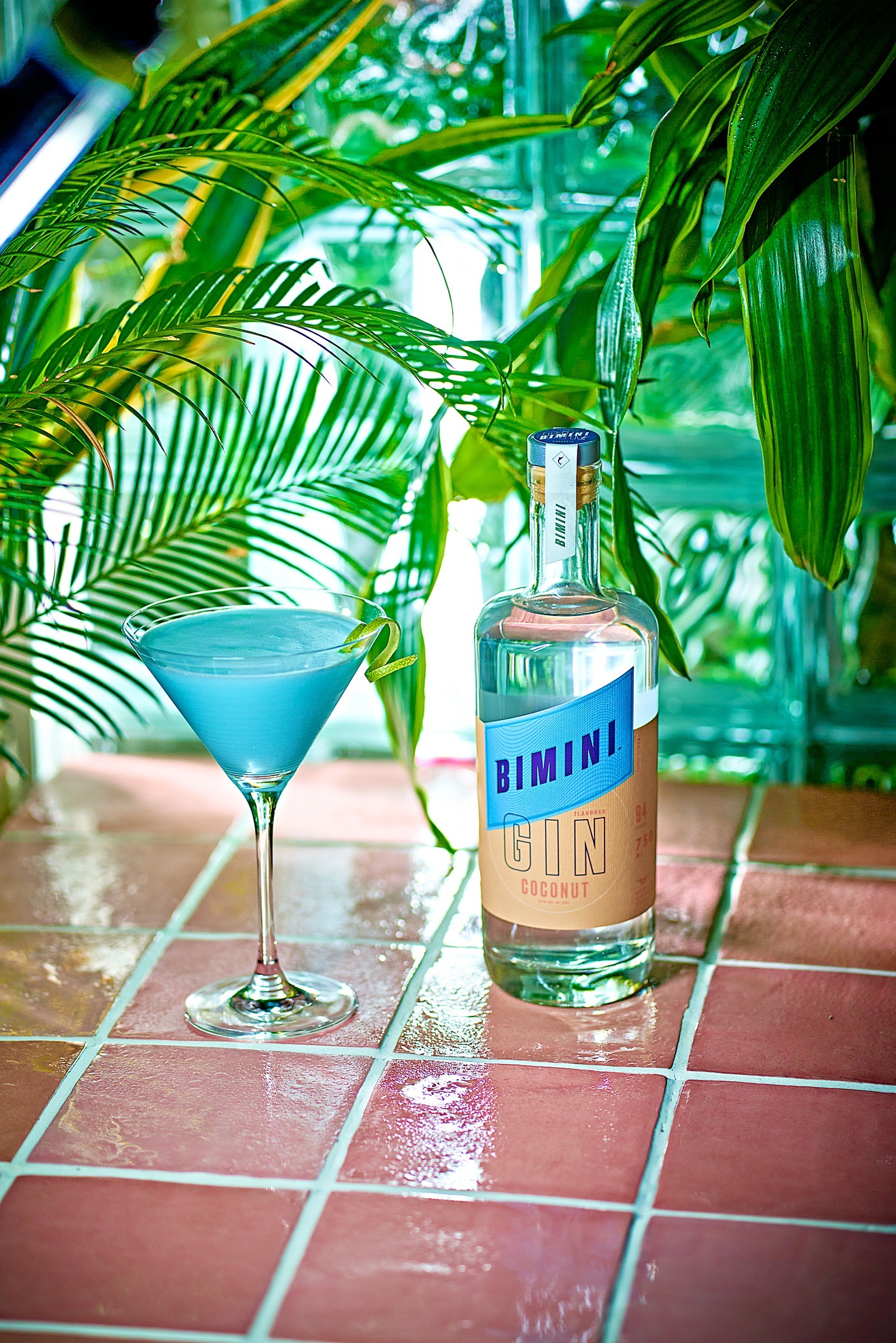Bimini Gin bottle and blue cocktail on a tiled patio surrounded by tropical greenery